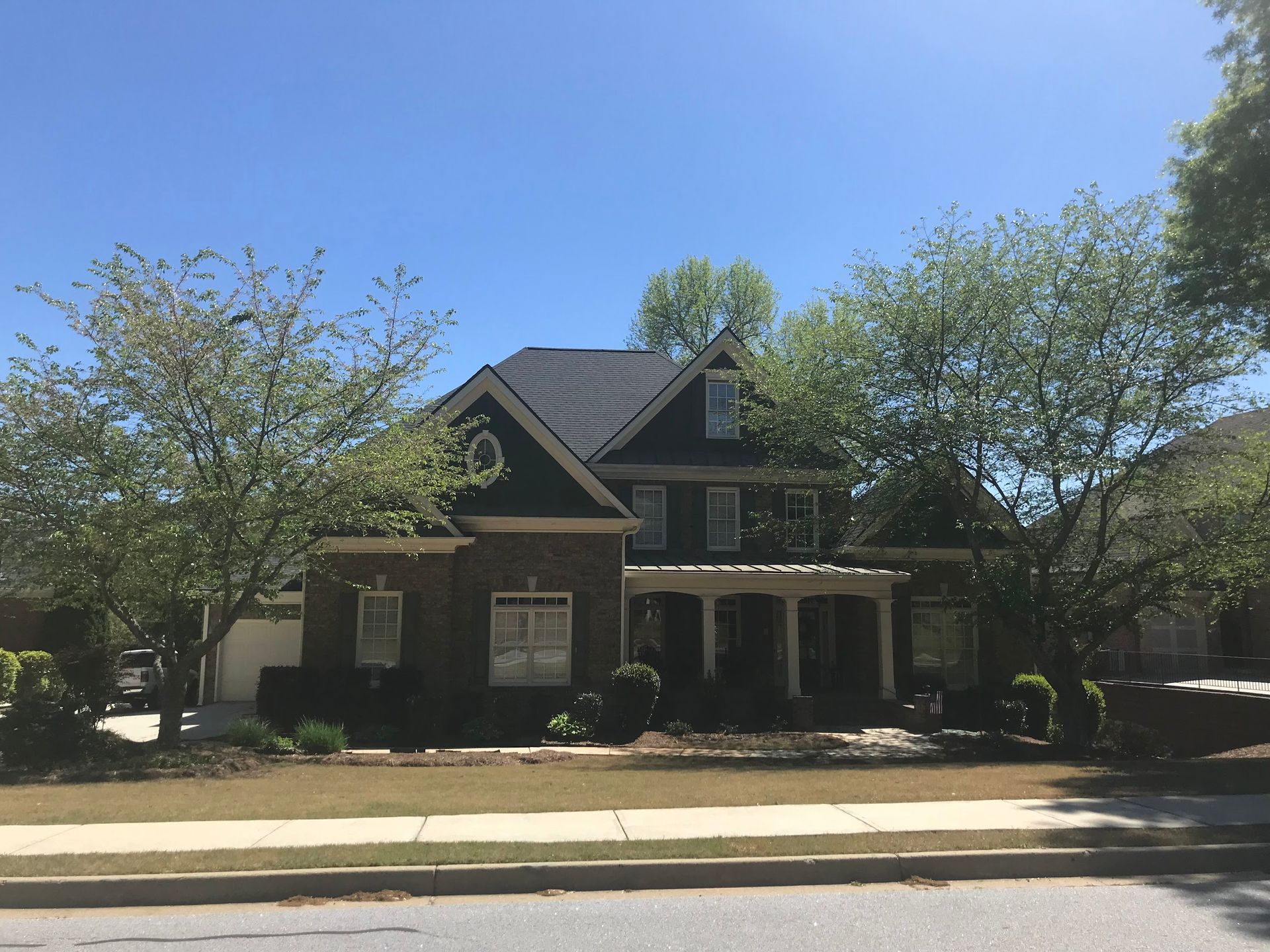Two-story brick house with dark roof and trim, trees in front, sunny day.