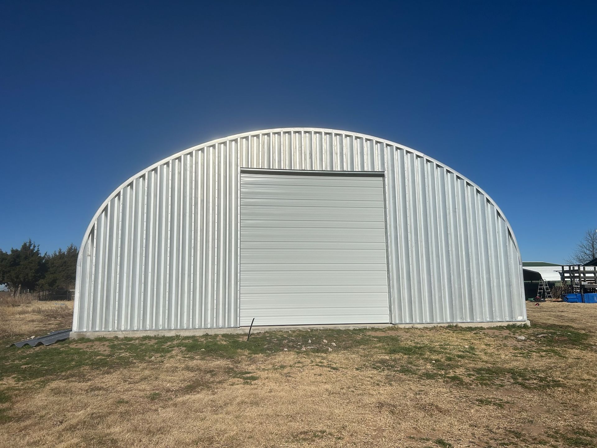 Metal Quonset hut with a closed garage door, set against a bright blue sky.