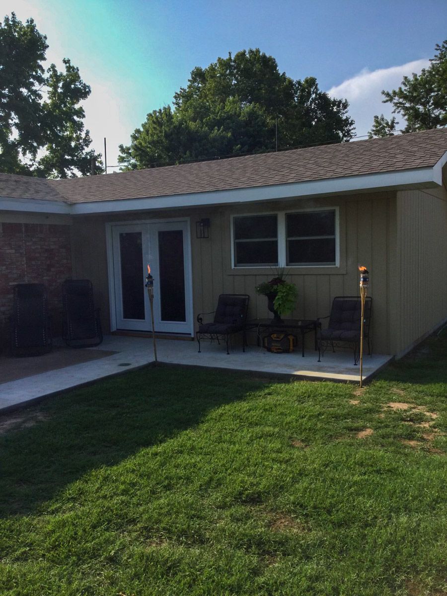 Exterior of a house with French doors, a window, and a small patio area with lawn in the foreground.