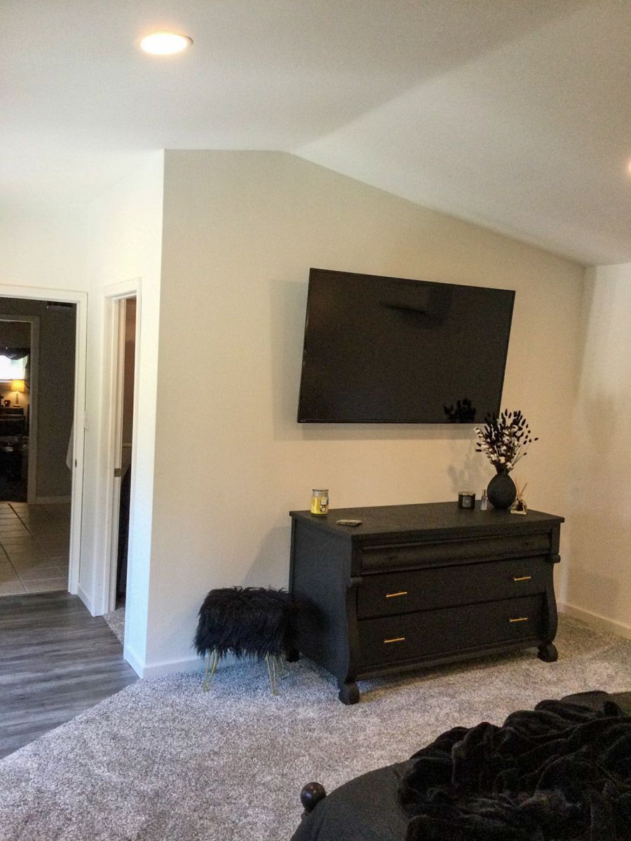 Bedroom with gray carpet, black dresser, and mounted TV. A black stool sits near the dresser.