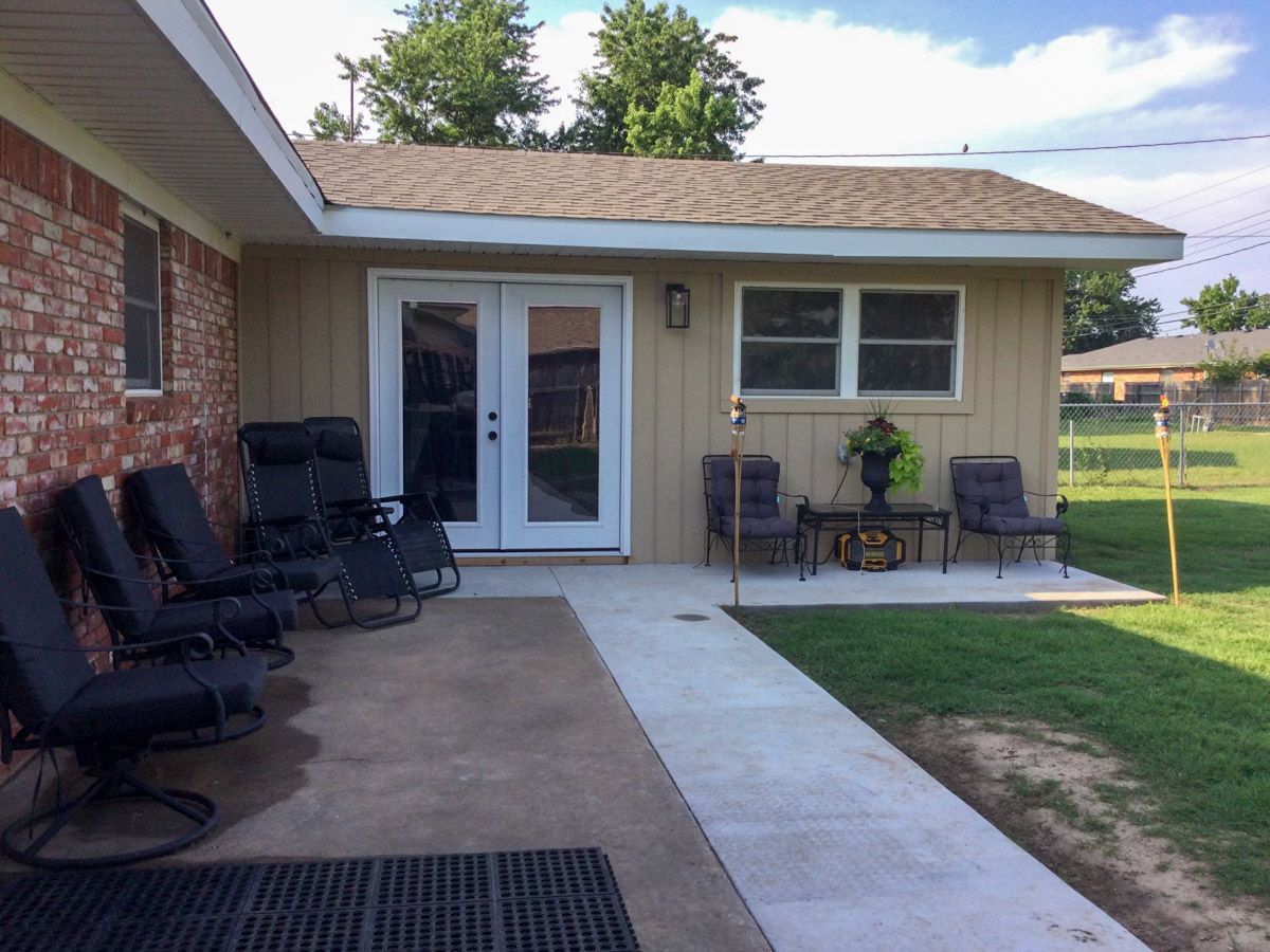 Back patio with chairs, French doors, small table with plants, and a walkway next to a grassy area.