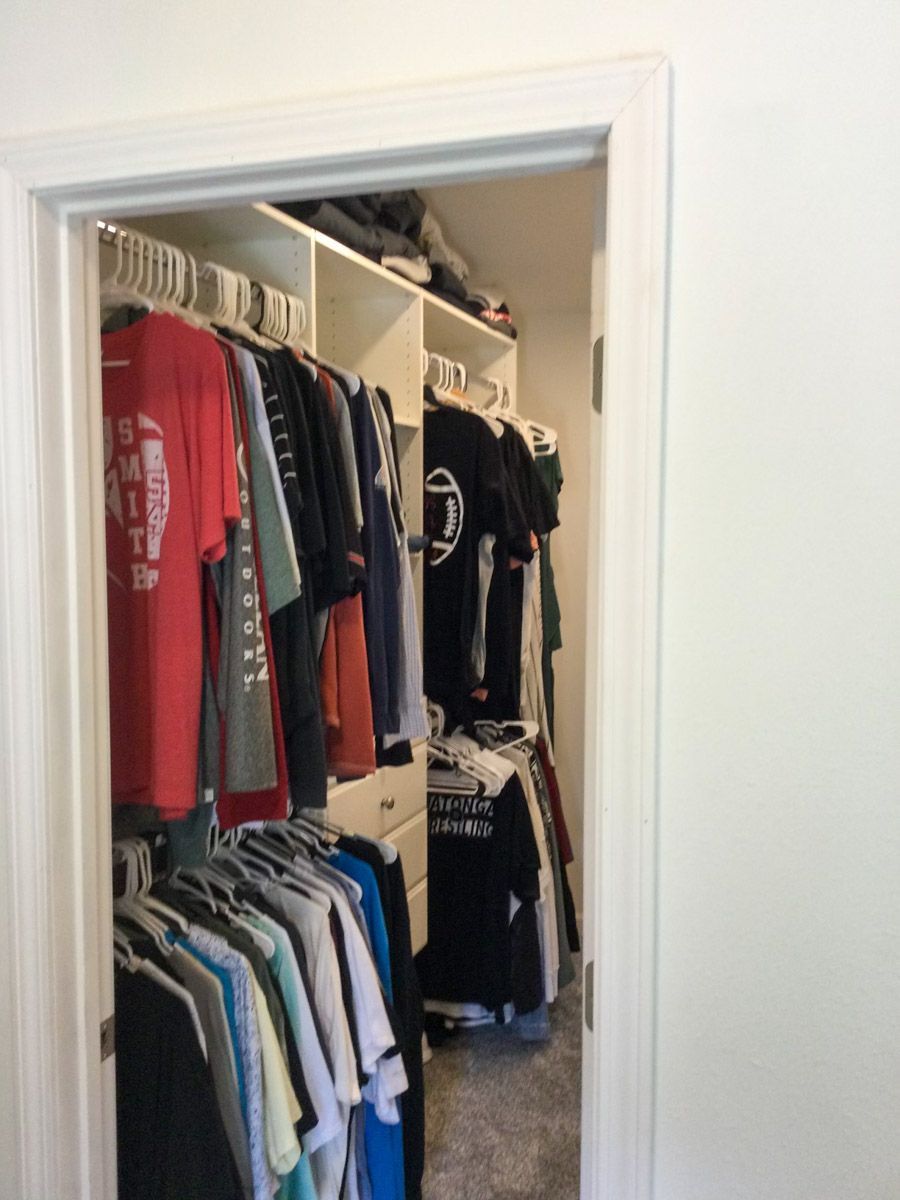 A closet filled with clothes, shirts and jackets hung on rods, with shelves above. White door frame.