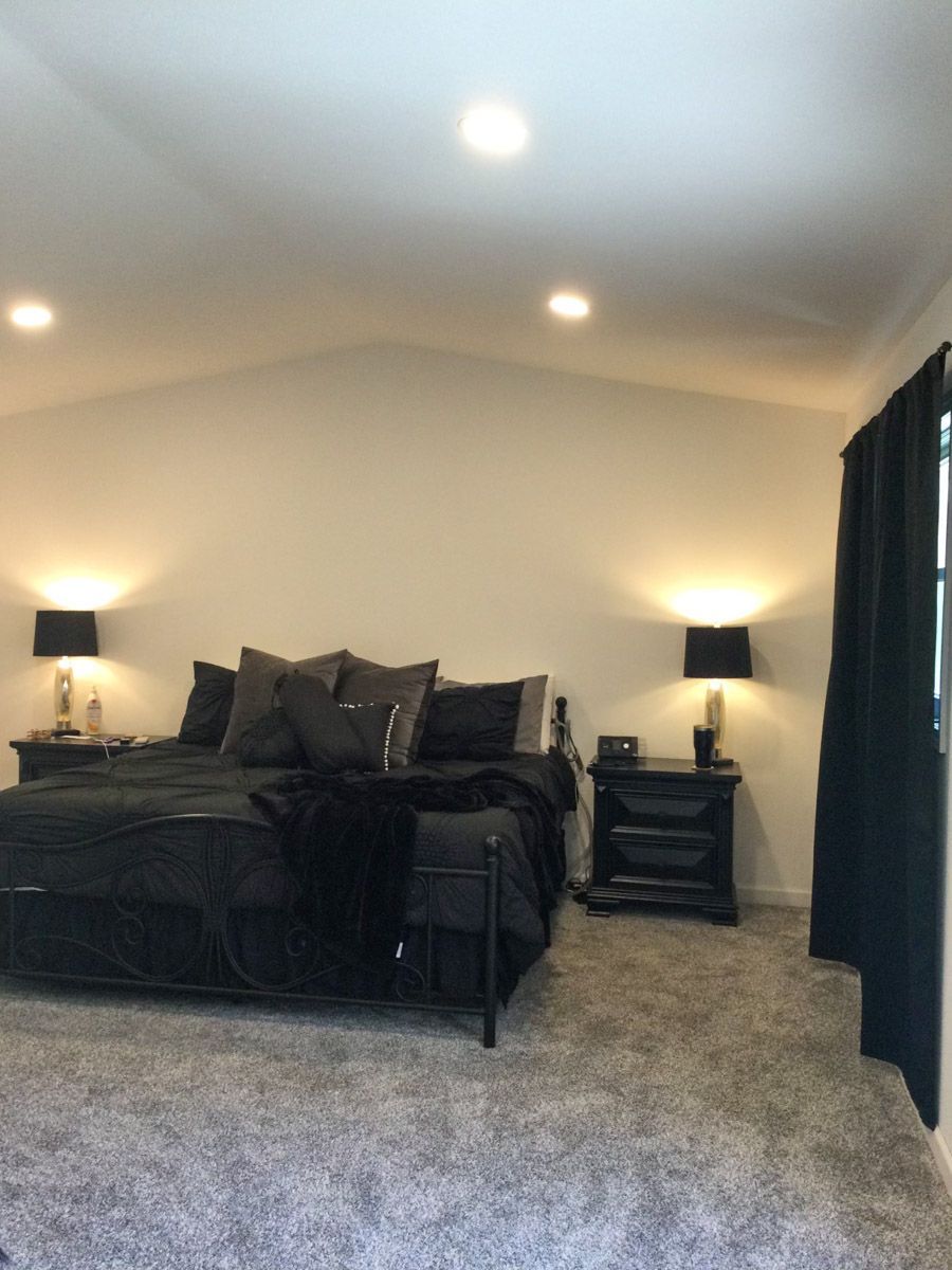 Bedroom with black bed, furniture, and accents. Gray carpet, white walls, and black curtains.