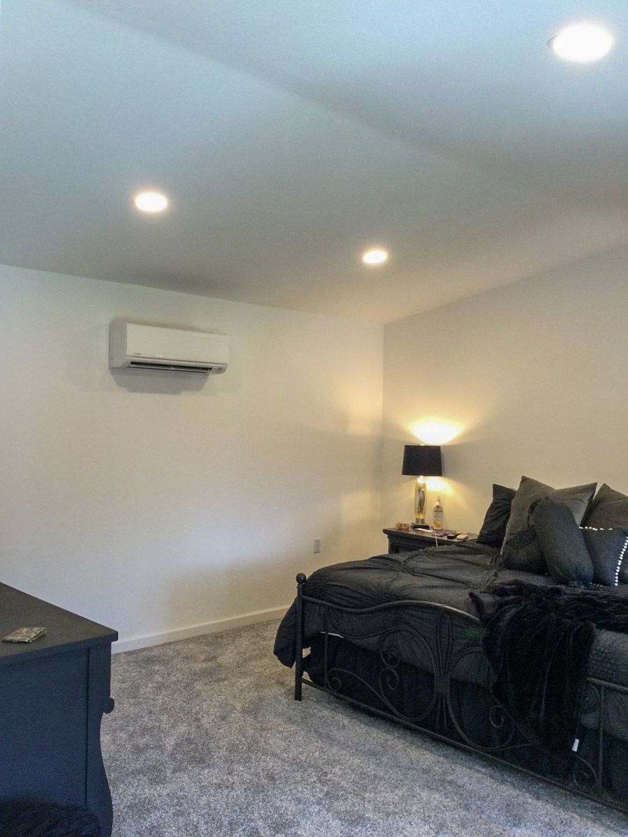 Bedroom with gray carpet, white walls, black bed, and air conditioning unit. Two recessed lights on ceiling.