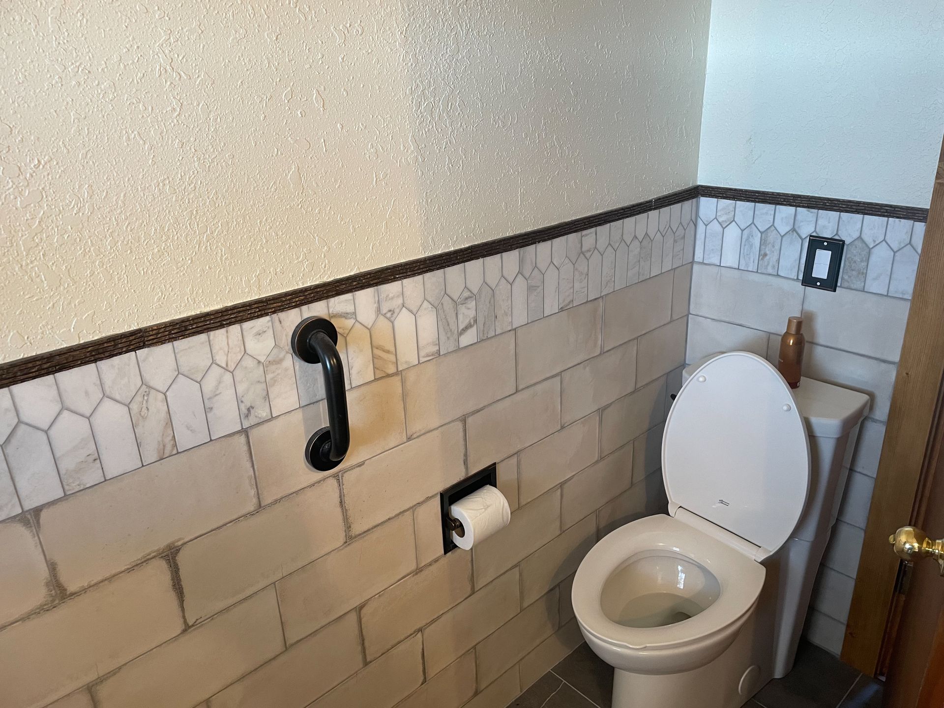 Bathroom with toilet, grab bar, and patterned tile.