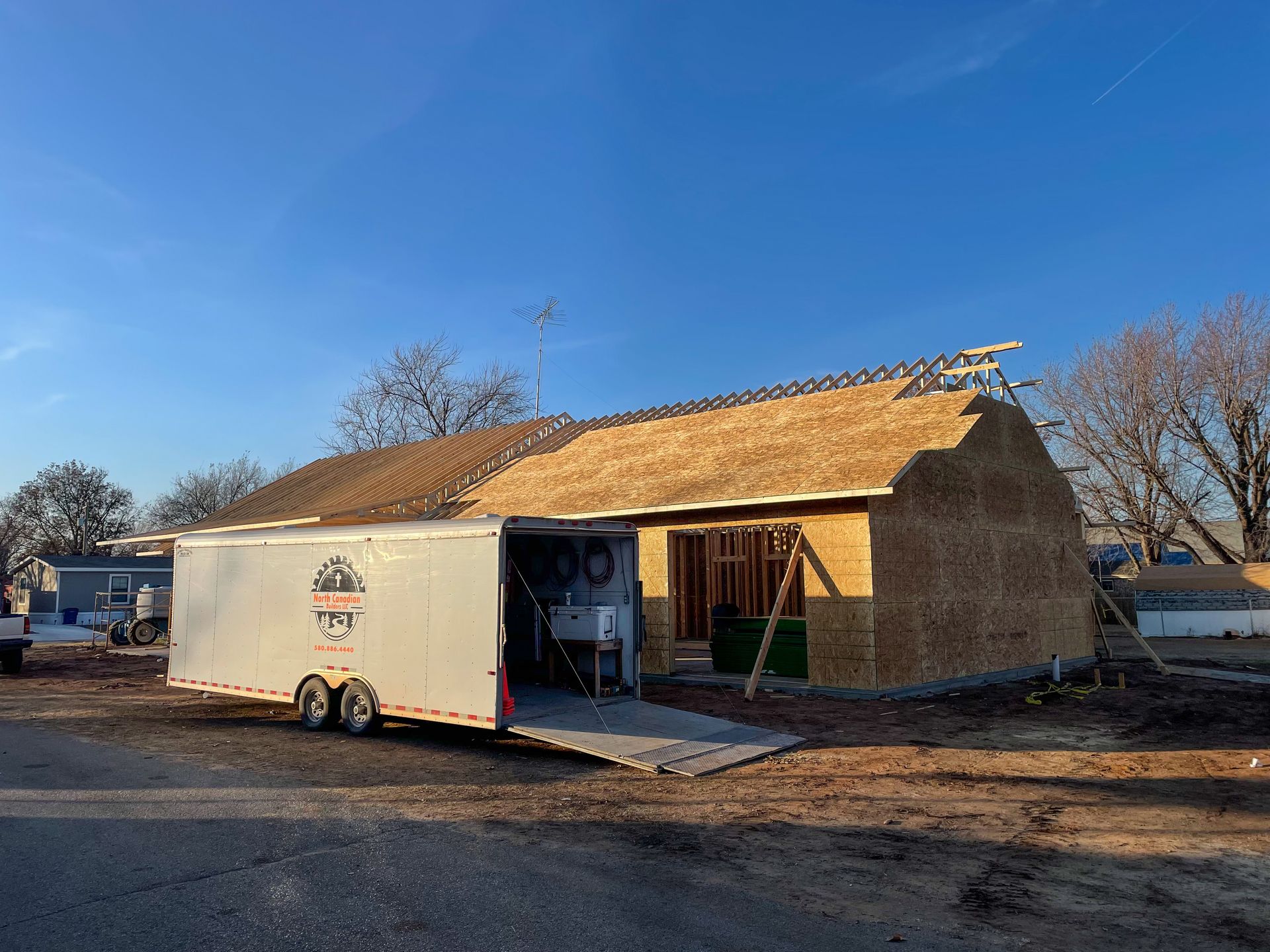 Construction site with a partially built house next to an open trailer under a clear blue sky.