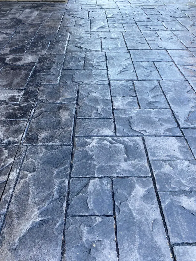 A close up of a concrete driveway with a brick pattern.