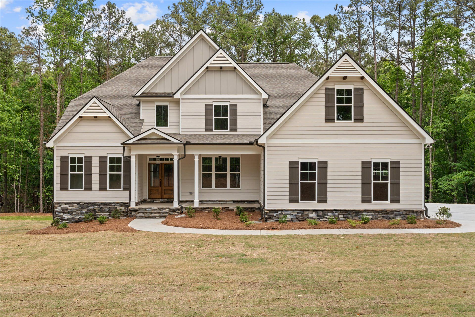 Two-story beige house with gray roof, front porch, and wooded background