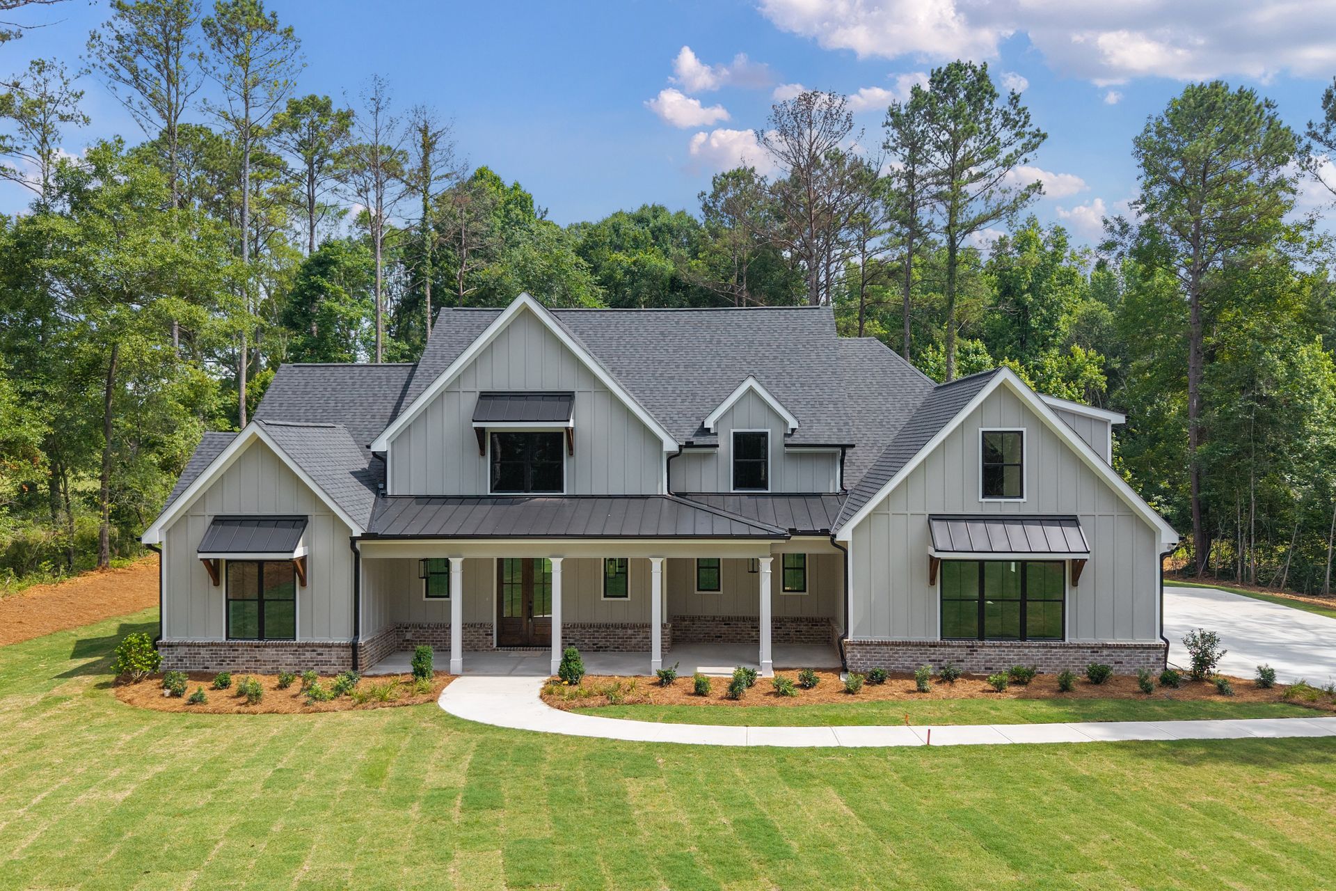 Gray suburban house with a front porch, dormer windows, and a large green lawn