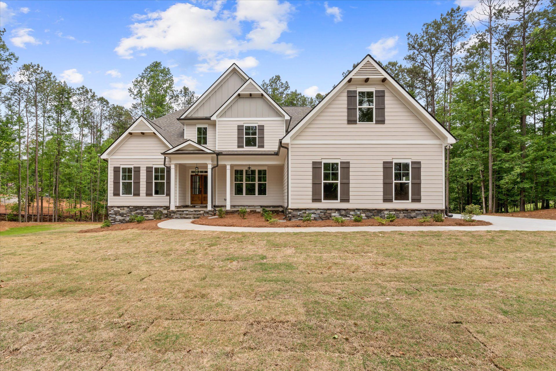 Front view of a beige suburban house with a front porch, surrounded by trees and a grassy yard.