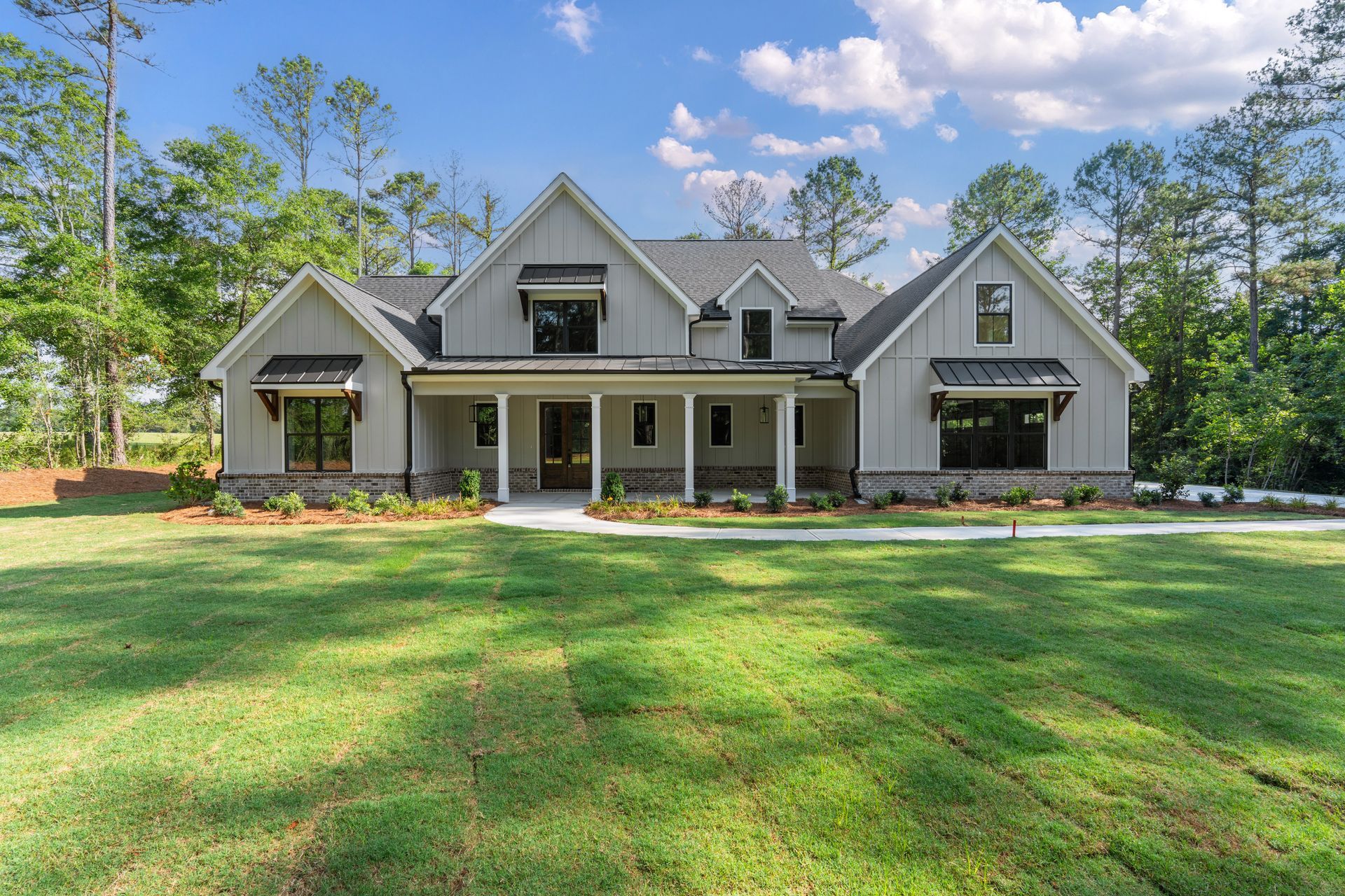 Large gray suburban house with a front porch, white trim, and a wide green lawn under a blue sky