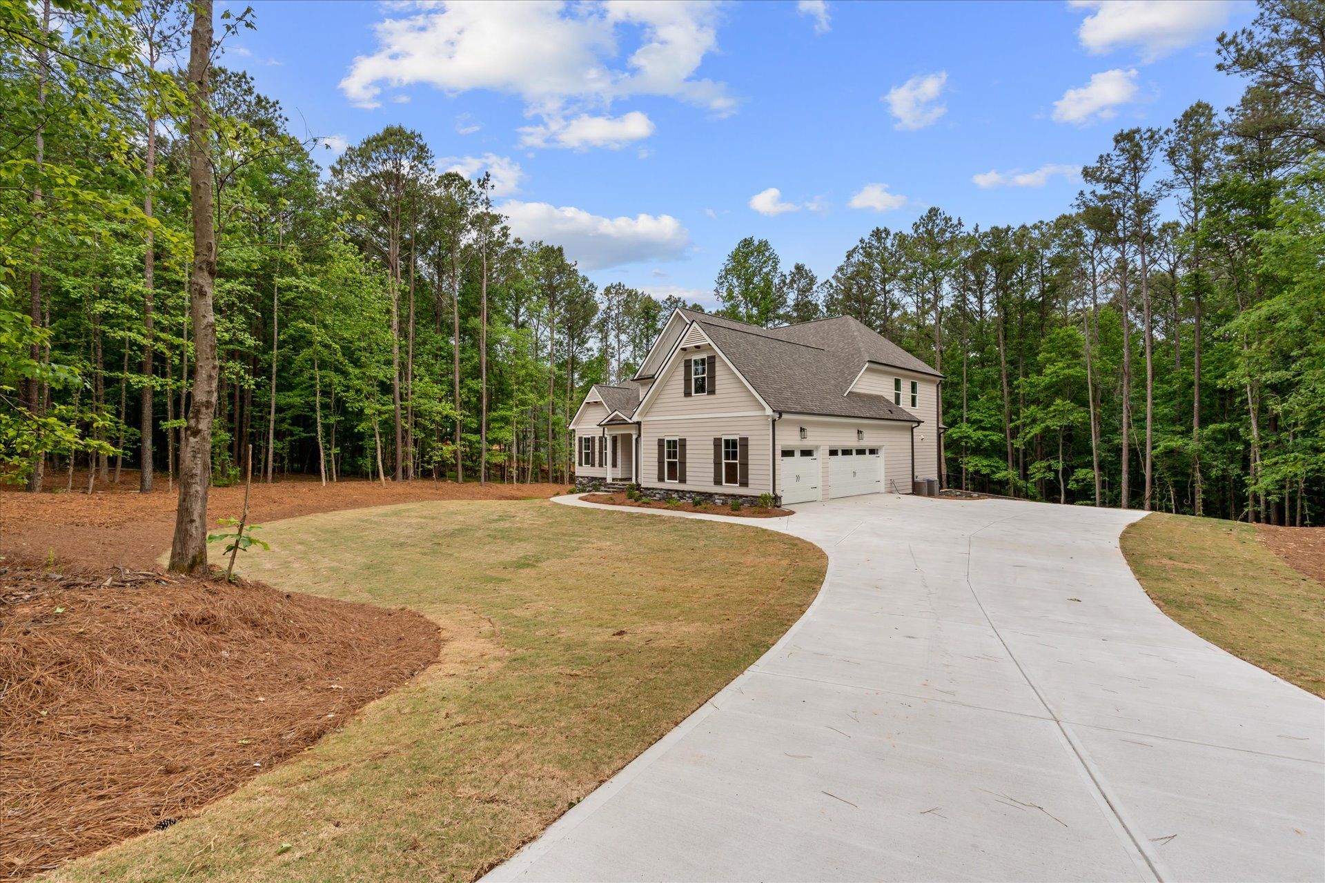 Suburban house with a long concrete driveway, surrounded by trees and a partly cleared yard