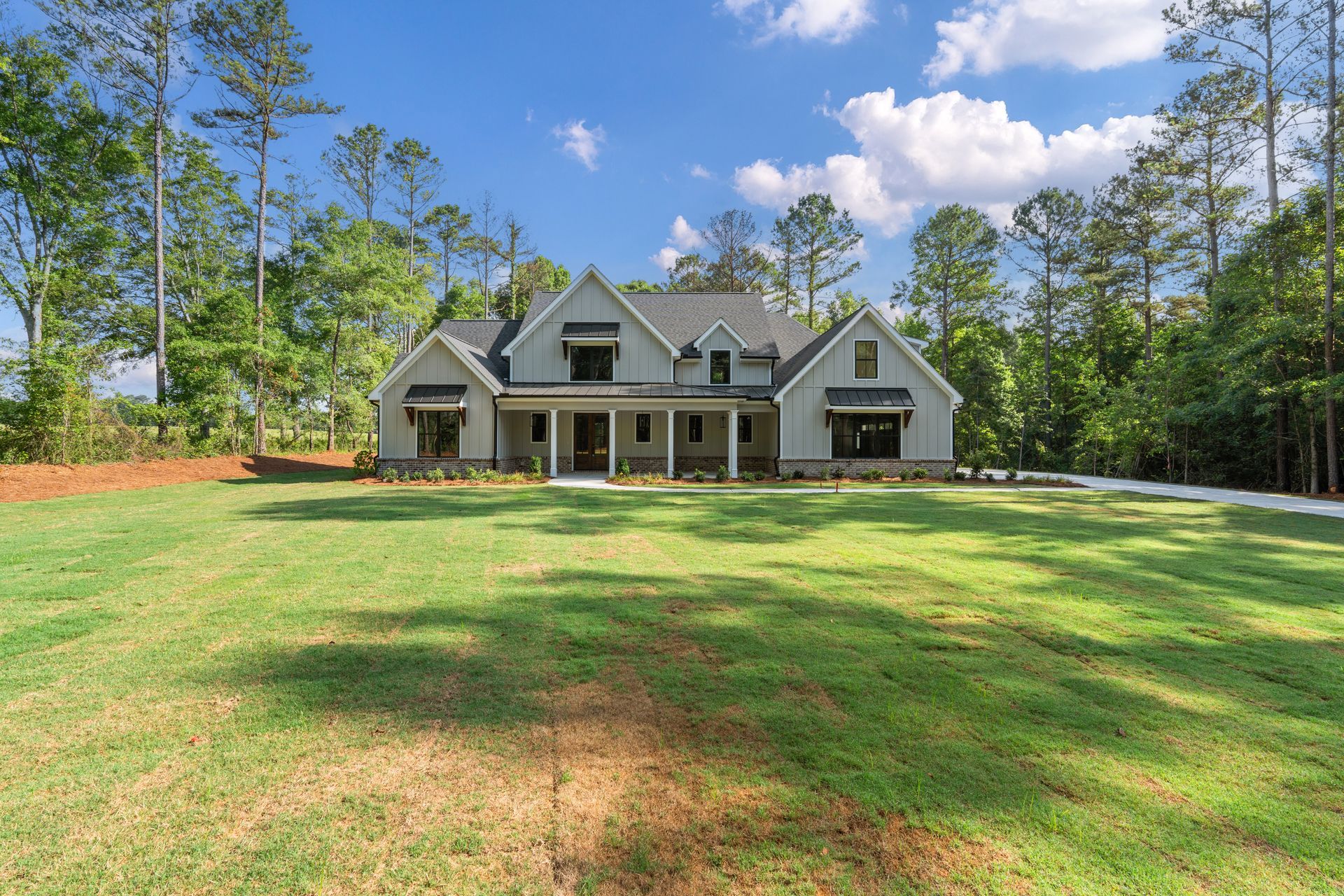 Large gray suburban house with a front porch, set in a sunny grassy yard surrounded by tall trees