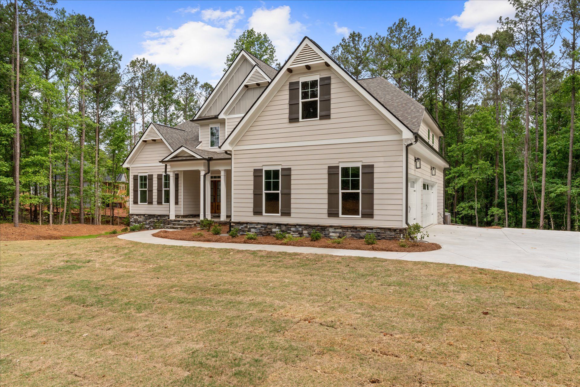 Suburban house with beige siding, gabled roof, front porch, and a paved driveway surrounded by trees