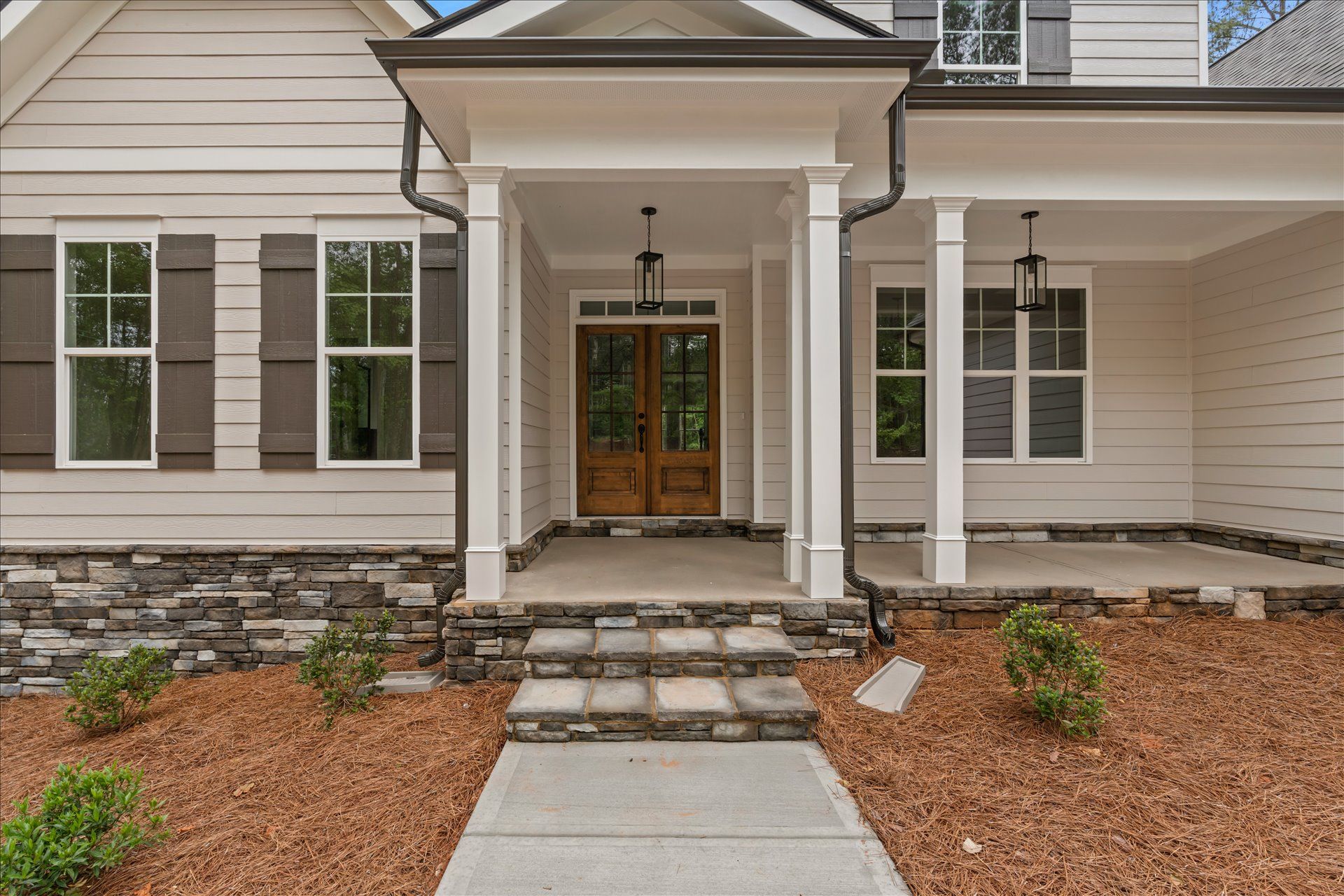 Front entrance of a beige house with stone steps, white columns, and a covered porch.