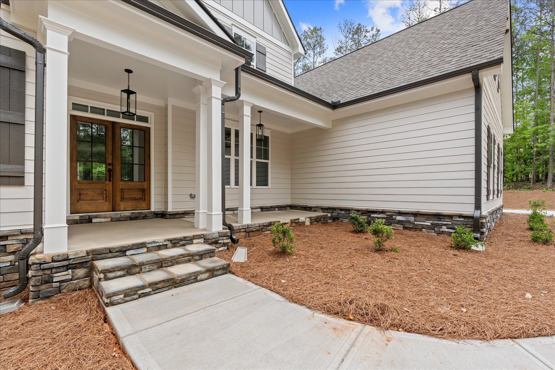 Front entrance of a white house with covered porch, steps, concrete walkway, and mulched landscaping