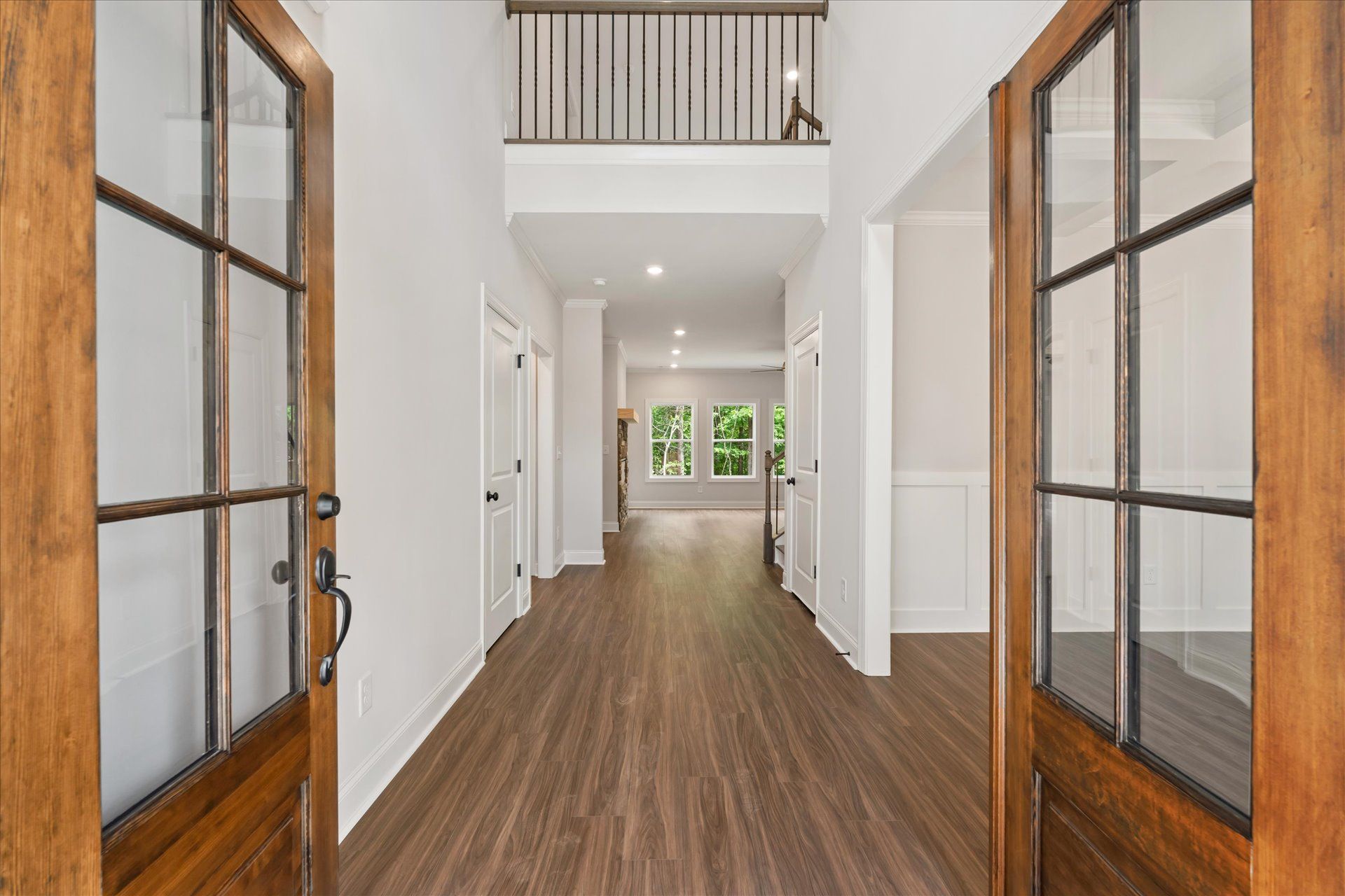 Bright hallway with wood floors, white walls, and glass-paneled double doors opening to a balcony view.