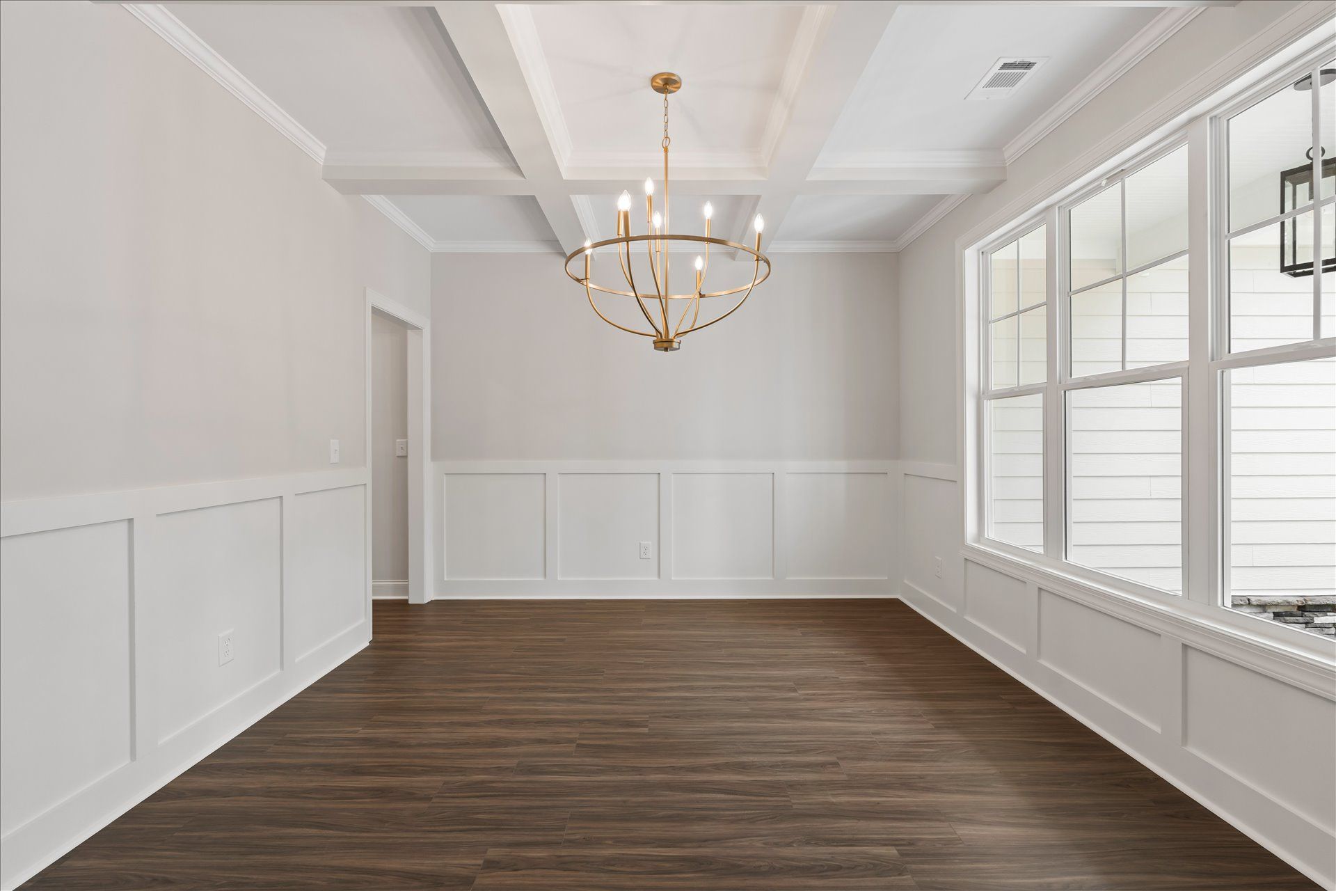 Empty bright dining room with white wainscoting, dark wood floor, chandelier, and large windows
