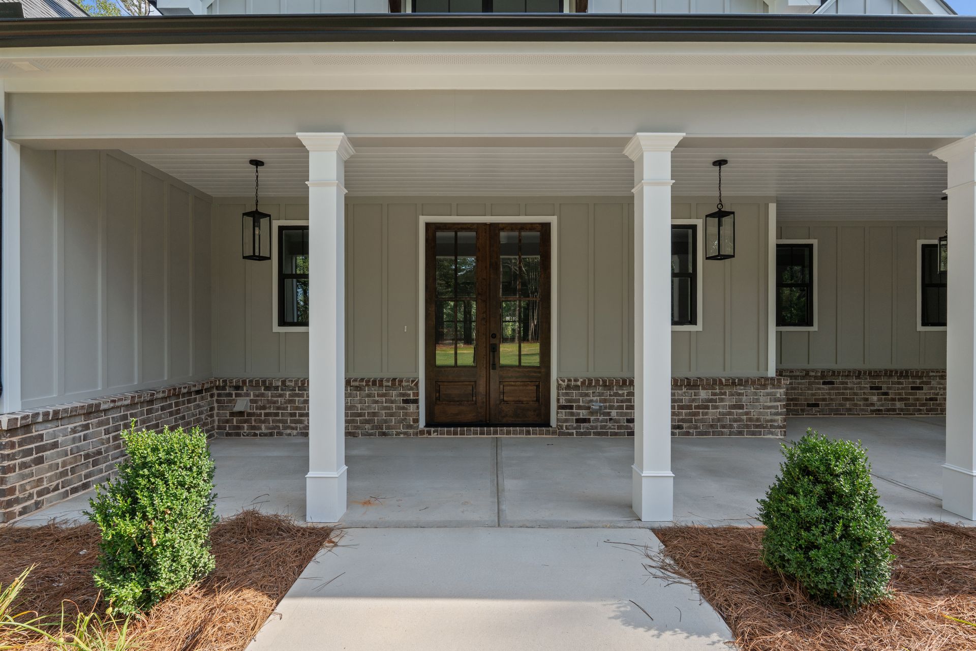 Covered front porch with white columns, double glass doors, and small shrubs lining the walkway