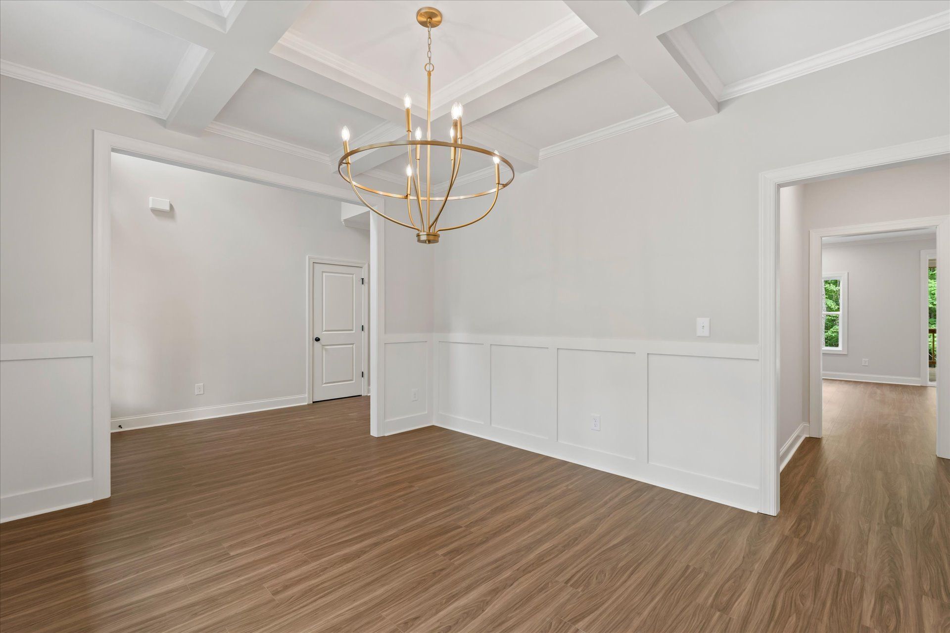Empty white dining room with coffered ceiling, gold chandelier, and wood flooring