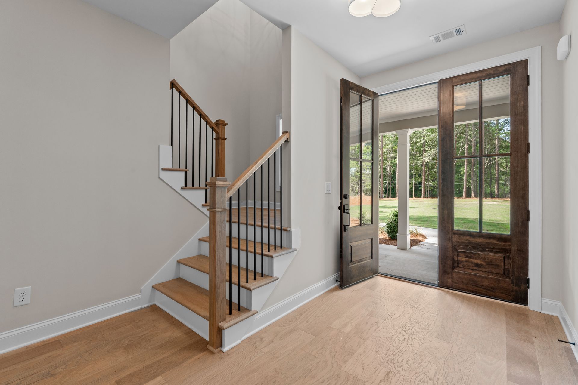 Bright foyer with staircase, beige carpet, and French doors opening to a wooded backyard.