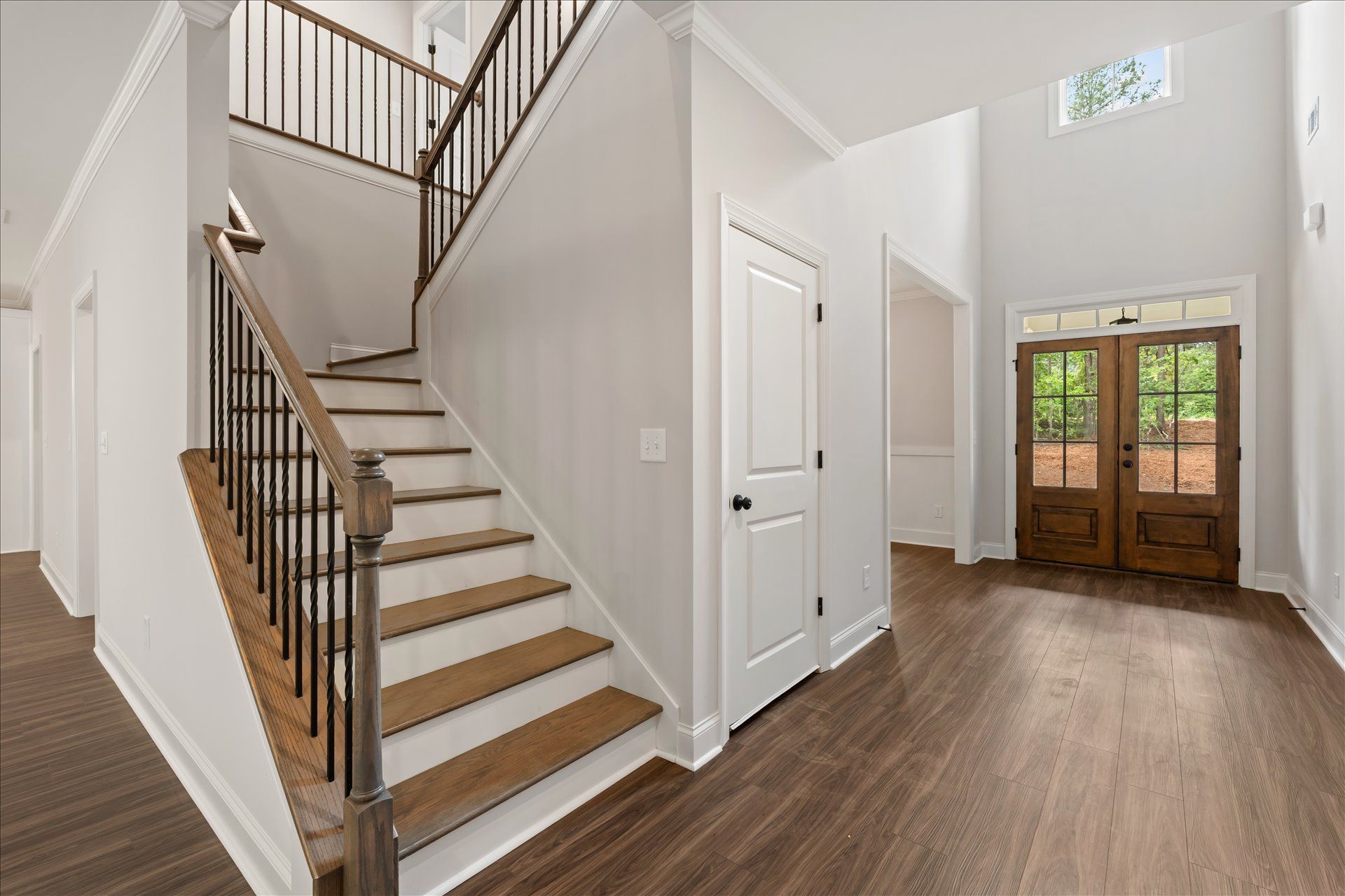 Bright foyer with wooden stairs, white walls, and front double doors leading to a hardwood floor entryway