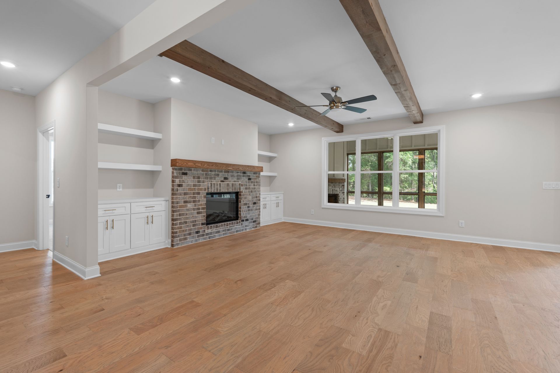 Spacious living room with wood floors, exposed beams, fireplace, and large window.