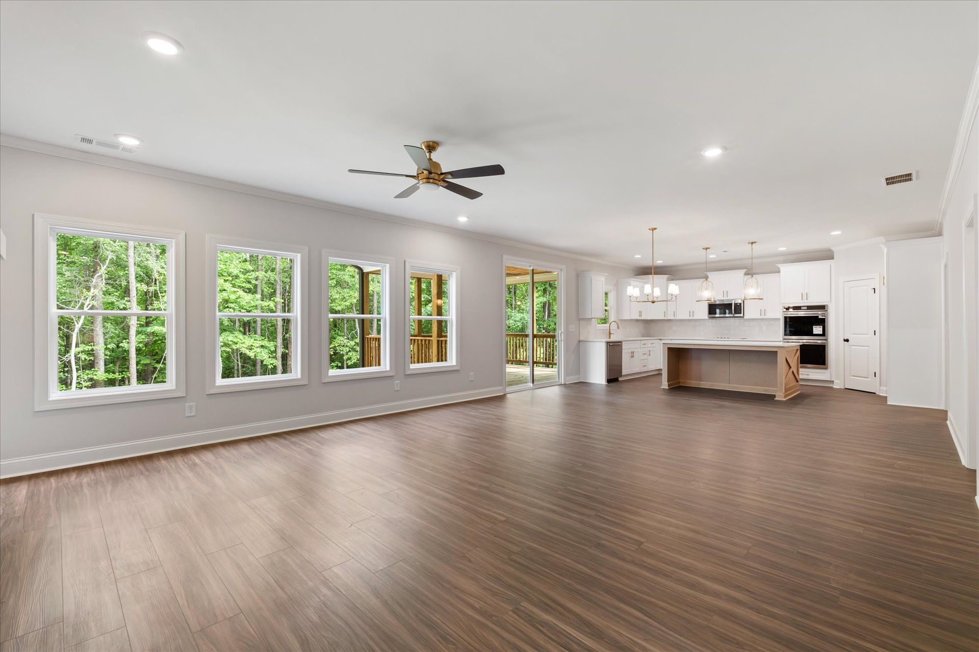 Spacious empty living room with wood floors, white walls, large windows, and an open kitchen.