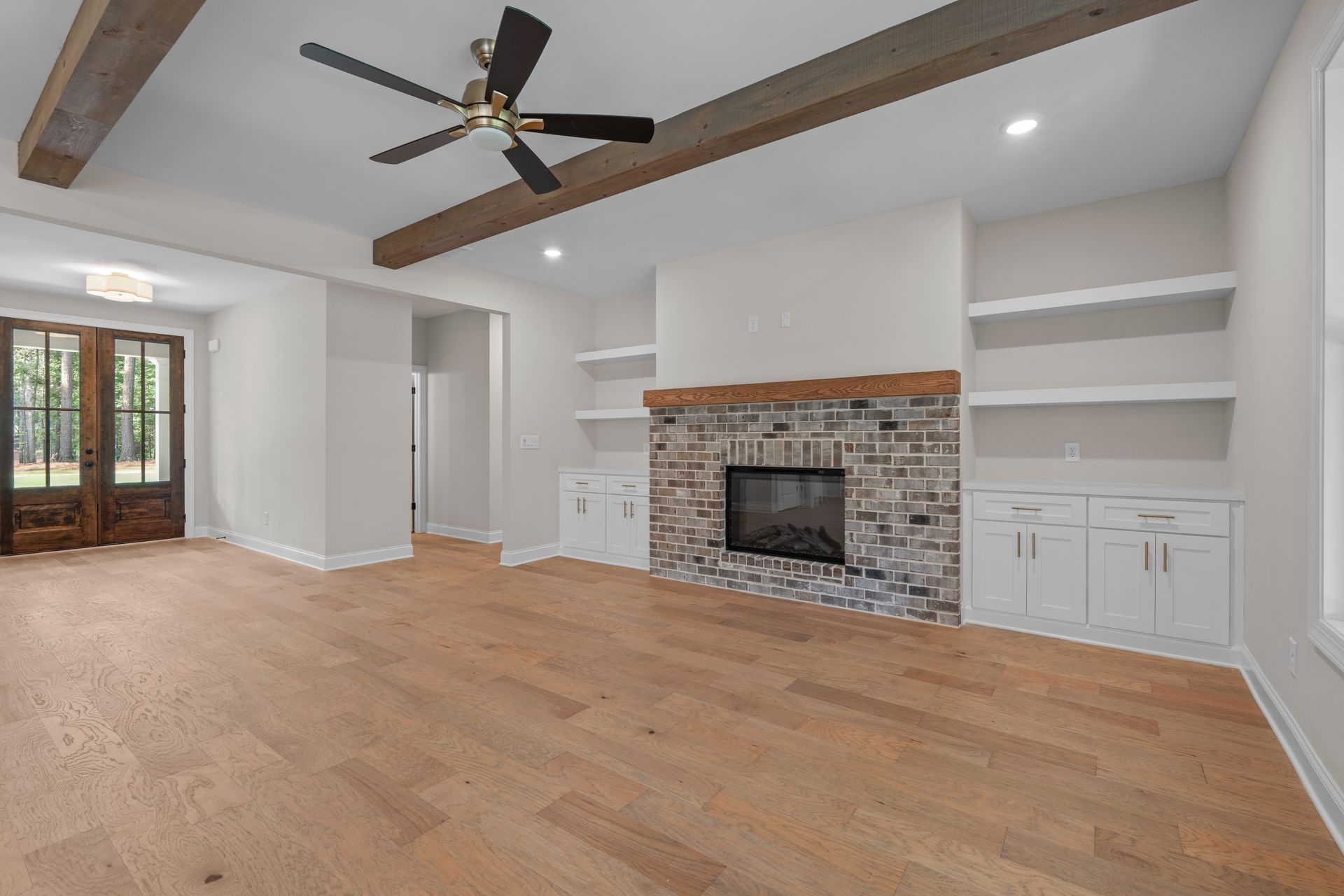 Spacious living room with hardwood floors, fireplace, built-in shelves, and a ceiling fan