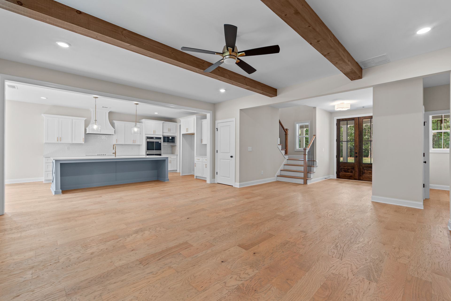Spacious modern living room with hardwood floors, exposed beams, ceiling fan, and open kitchen.