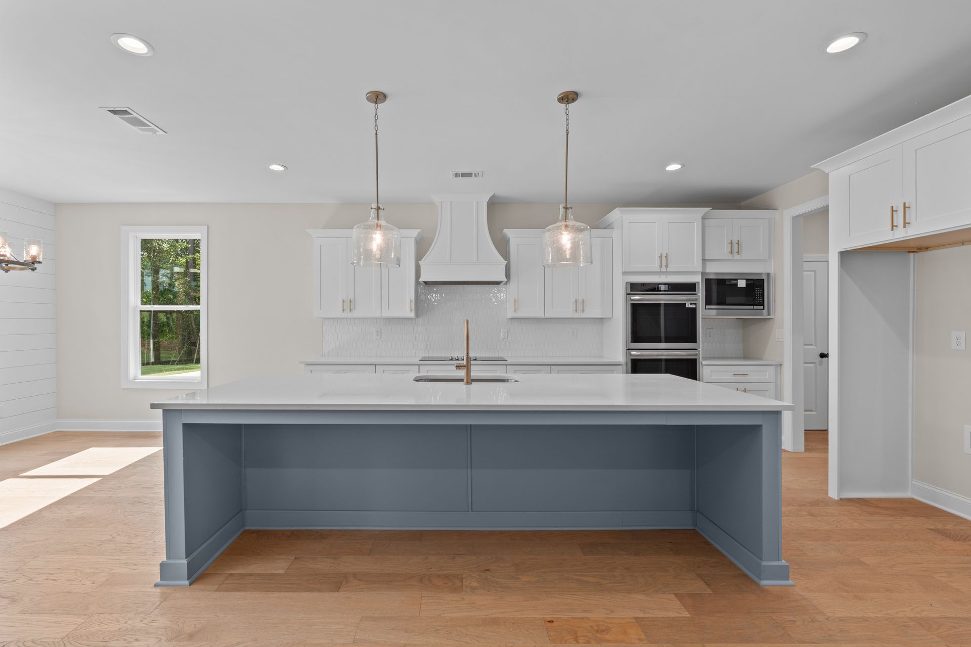 Bright modern kitchen with blue island, white cabinets, stainless appliances, and hardwood floors.