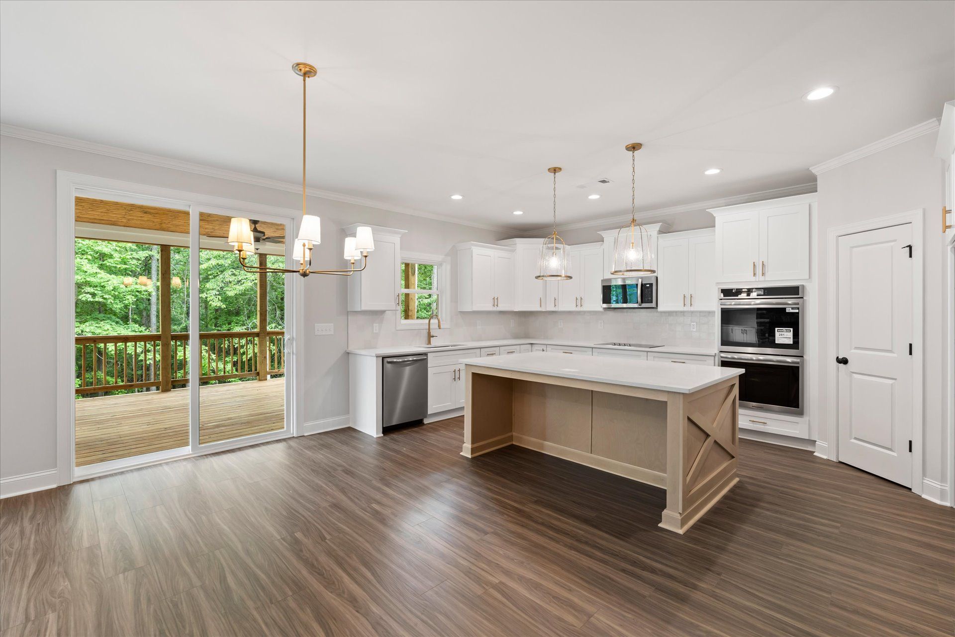 Bright modern kitchen with white cabinets, island, stainless appliances, and sliding glass doors to a wooded deck