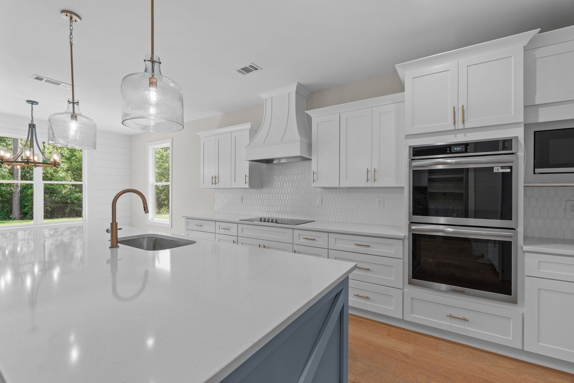 Bright white modern kitchen with island, pendant lights, and built-in double ovens