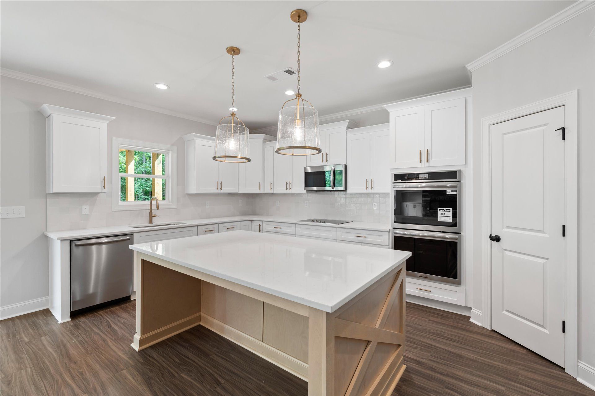 Bright white modern kitchen with island, pendant lights, dark wood floors, and built-in oven