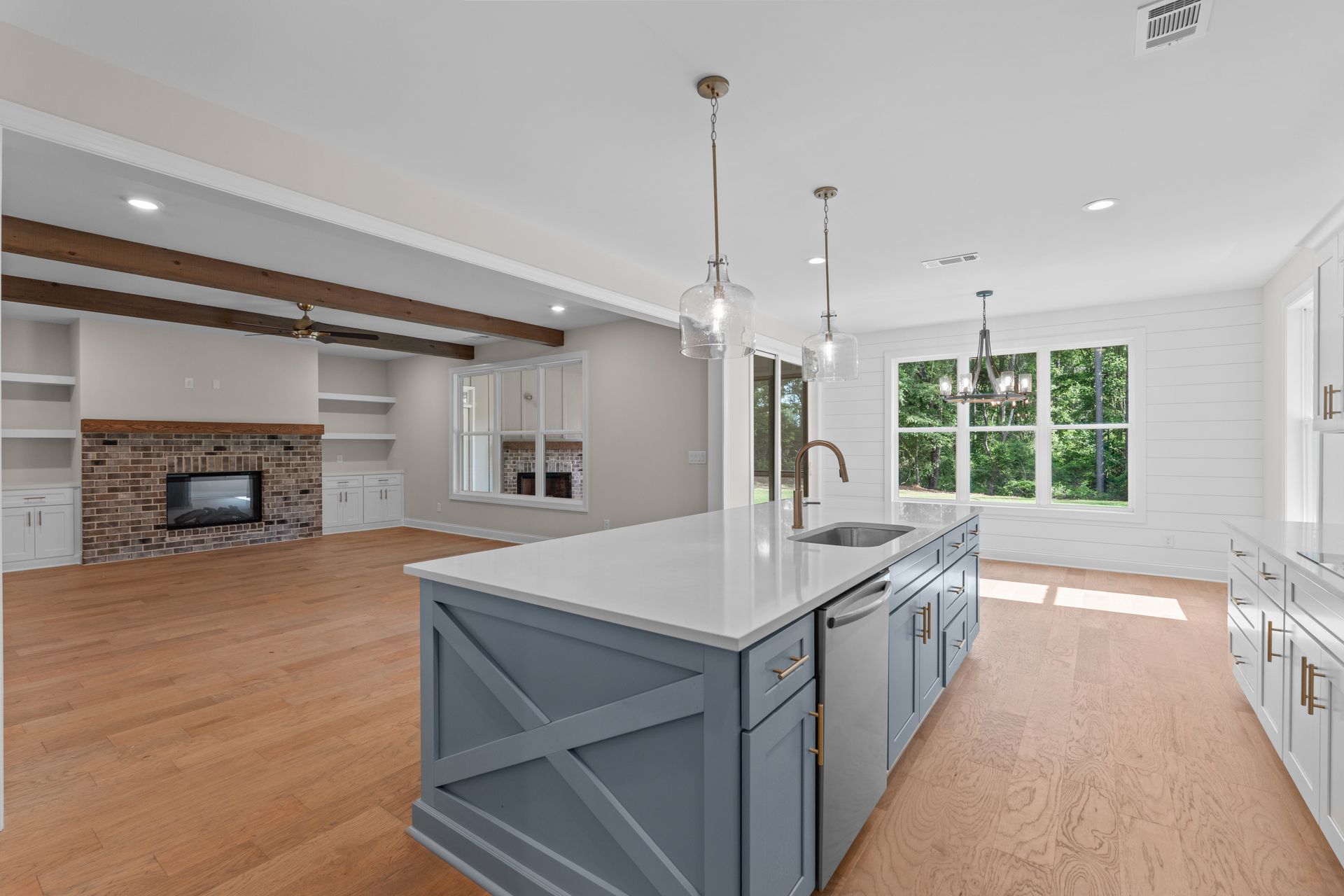 Bright open kitchen with gray island, brick fireplace, hardwood floors, and large windows