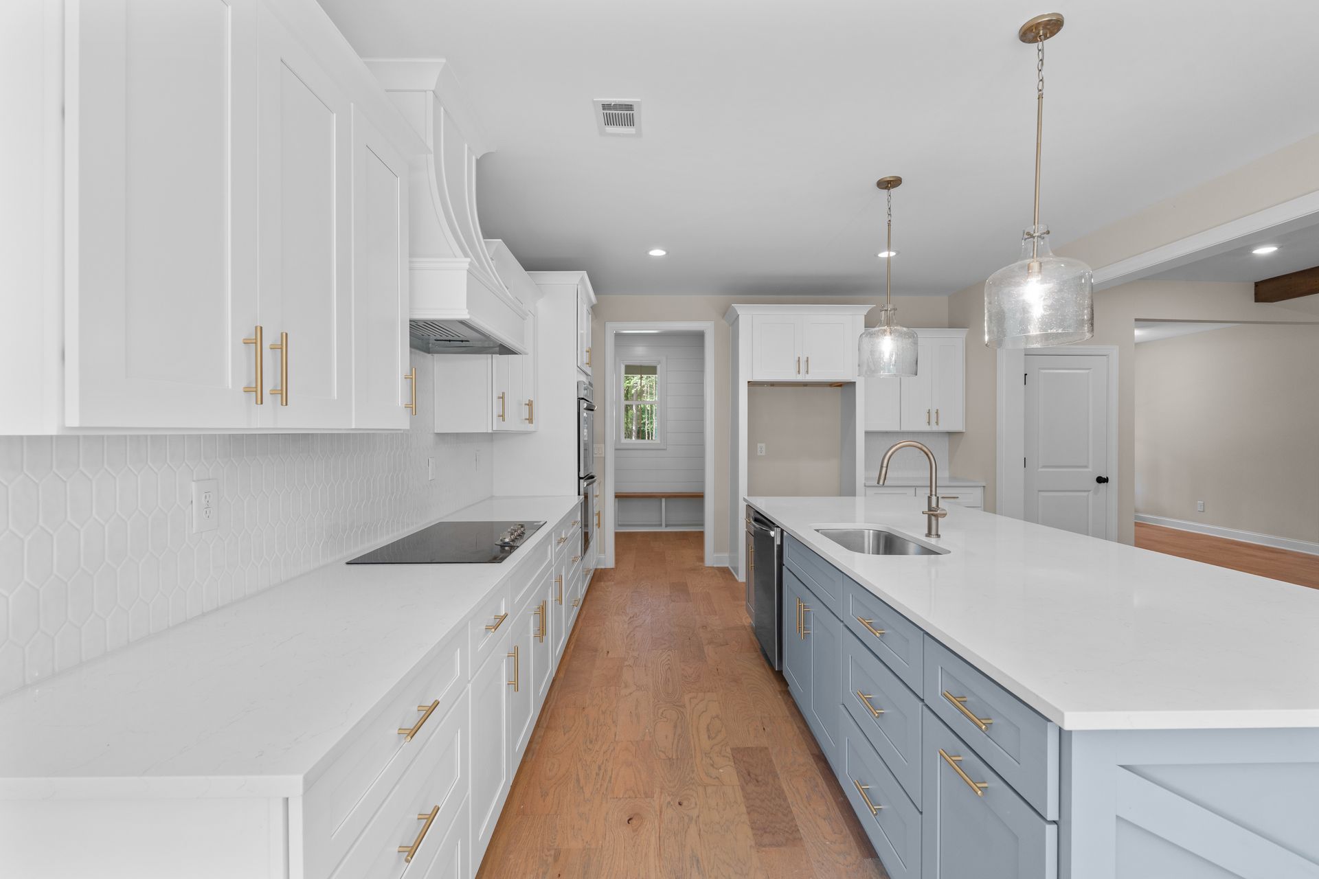 Bright modern kitchen with white cabinets, blue island, wood floors, and pendant lights