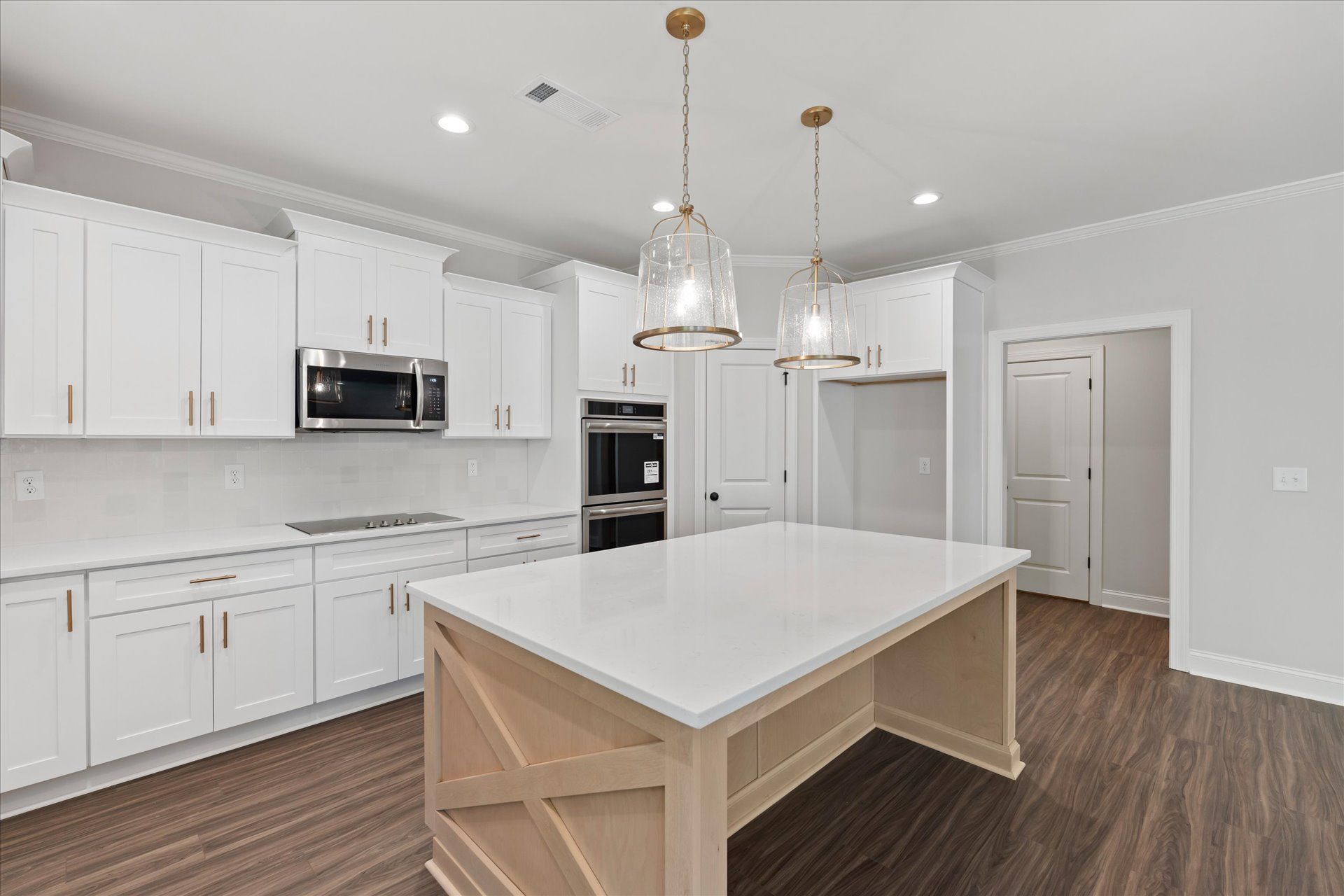 Bright modern kitchen with white cabinets, large island, pendant lights, and wood floors