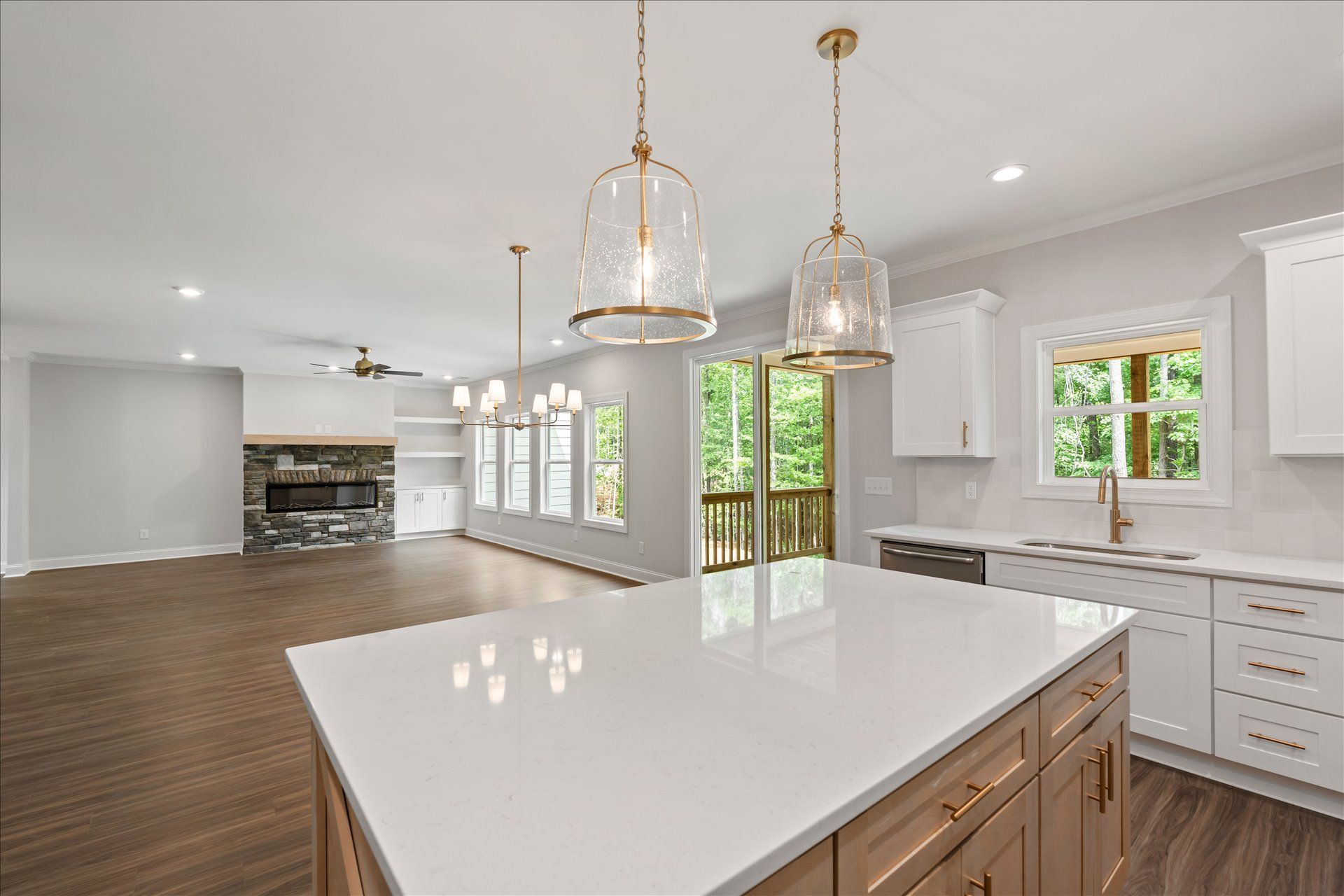 Modern kitchen with large white island, pendant lights, wood floors, and open view to living area and windows