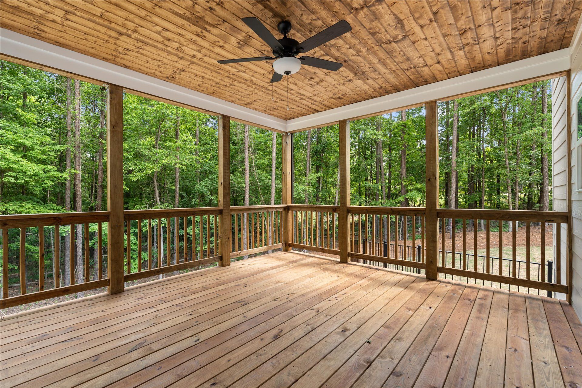 Covered wooden deck with screened railings and a ceiling fan, surrounded by trees