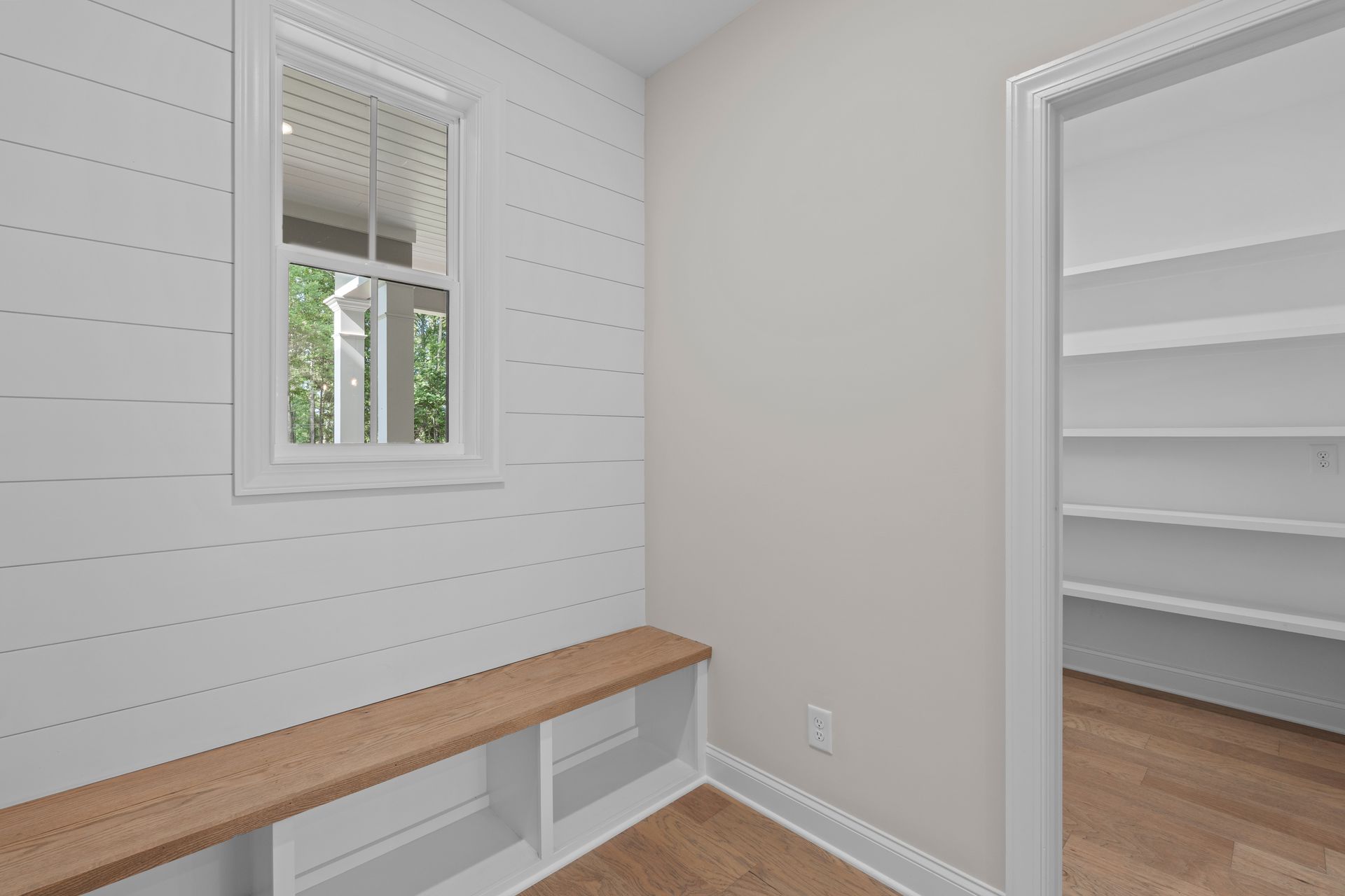 Small white entryway with bench, window, and open closet shelves.
