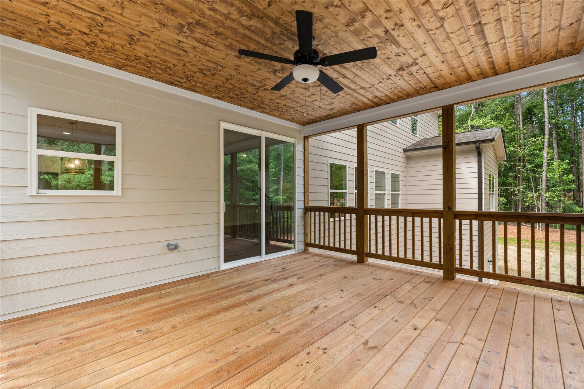 Covered wooden deck with ceiling fan, sliding glass door, and railing overlooking a yard