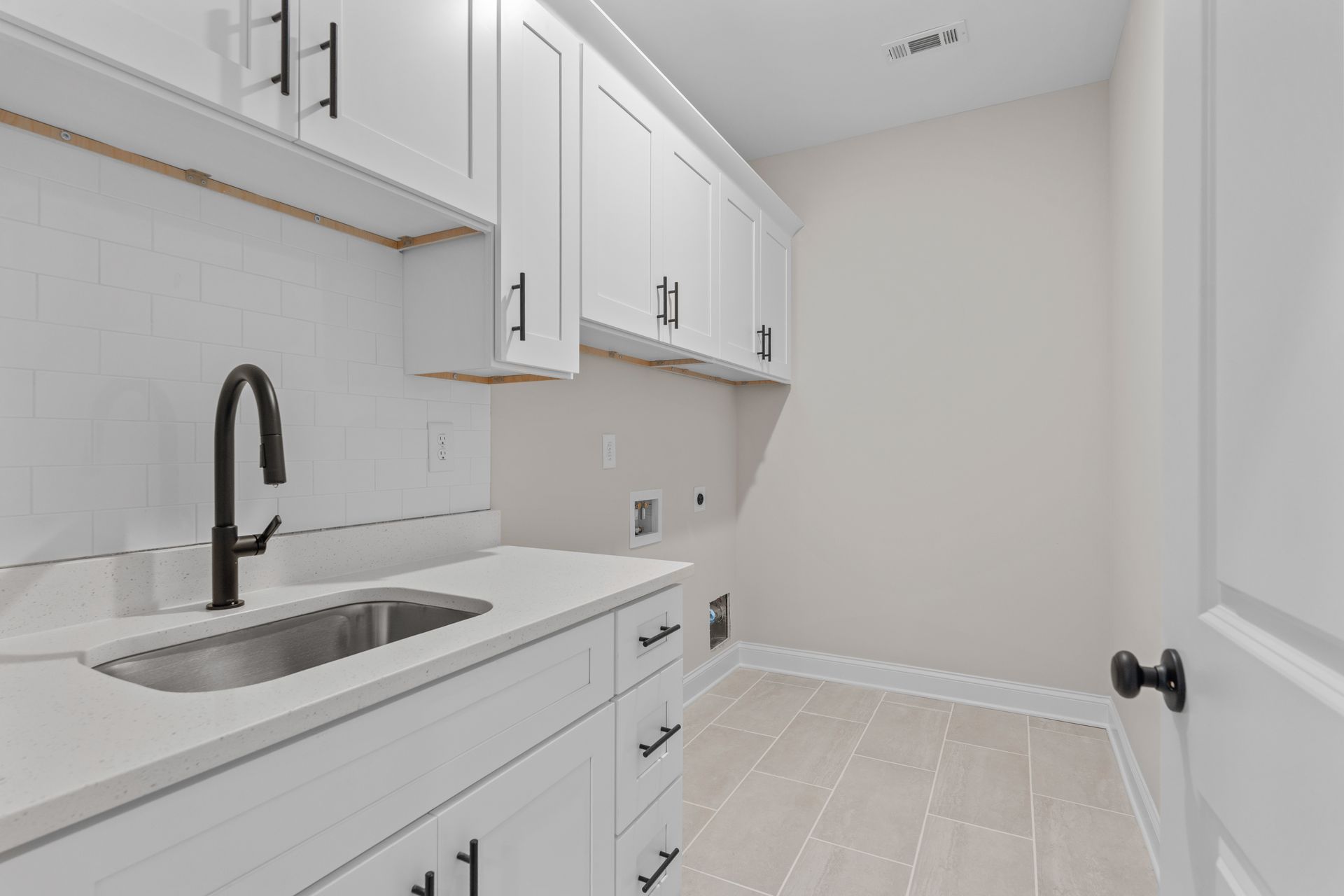 Bright white galley laundry room with sink, black faucet, cabinets, and tiled floor