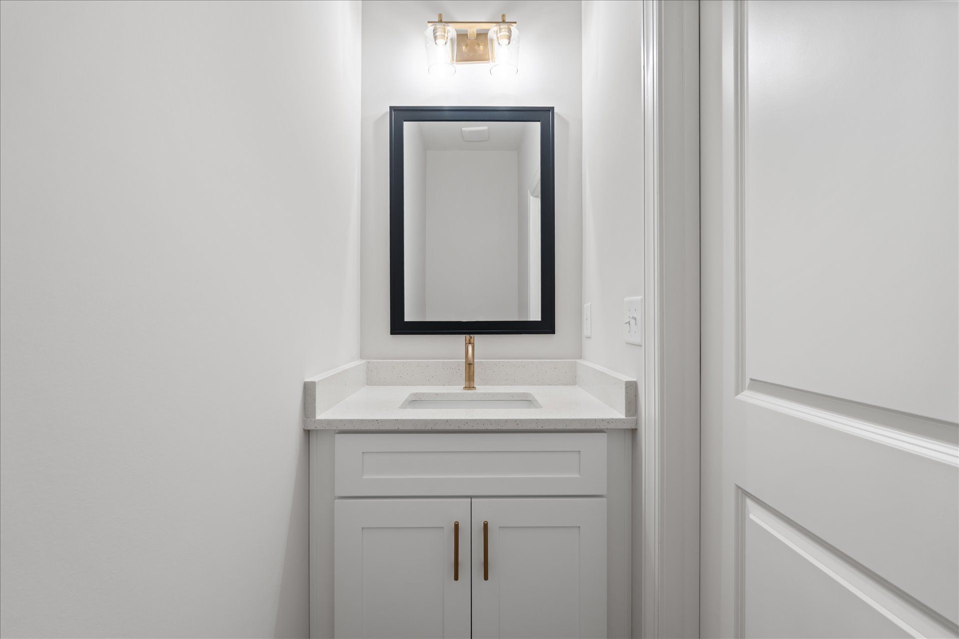 Small white bathroom vanity with mirror and wall sconce in a narrow hallway.