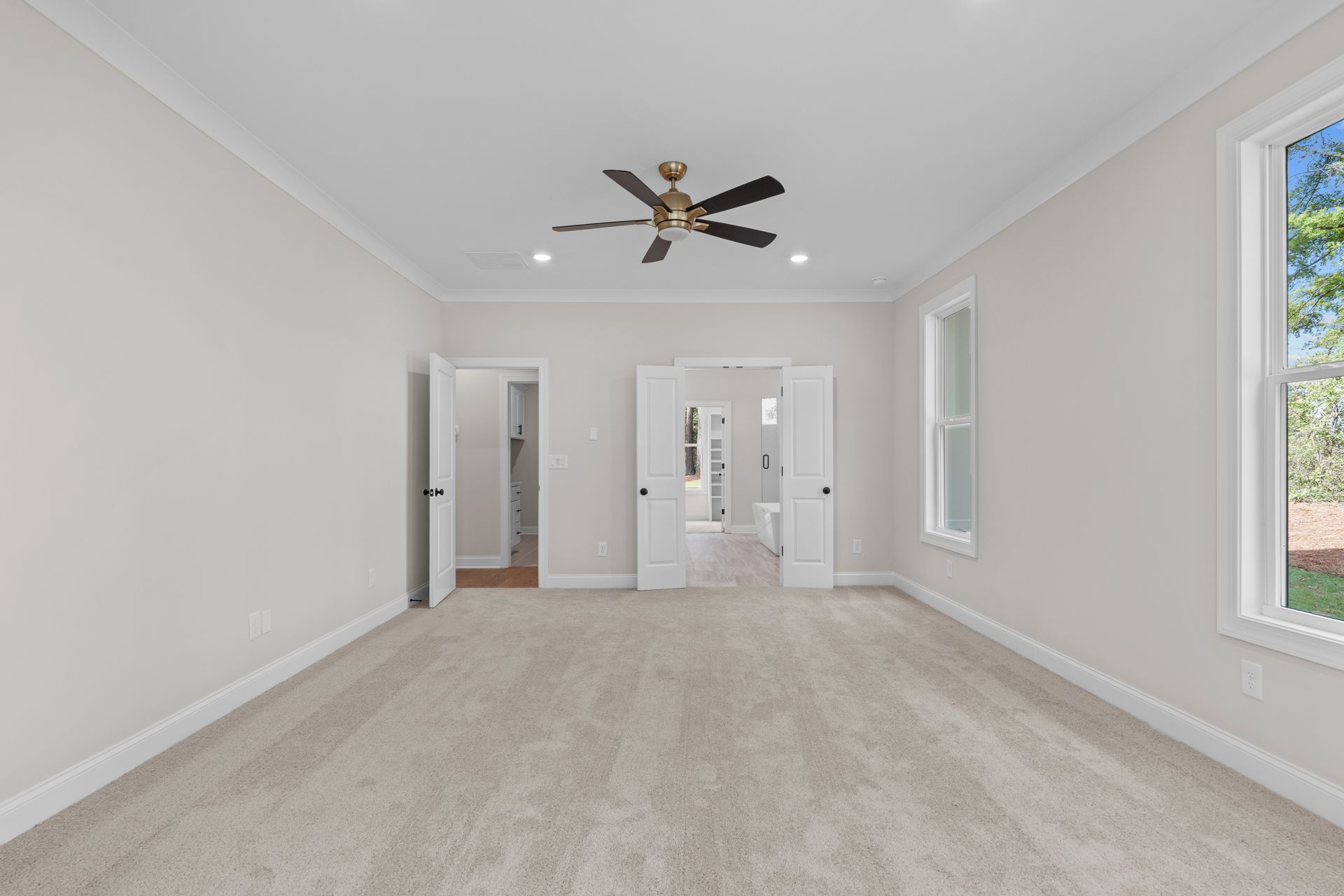 Empty beige living room with vaulted ceiling, ceiling fan, and large windows