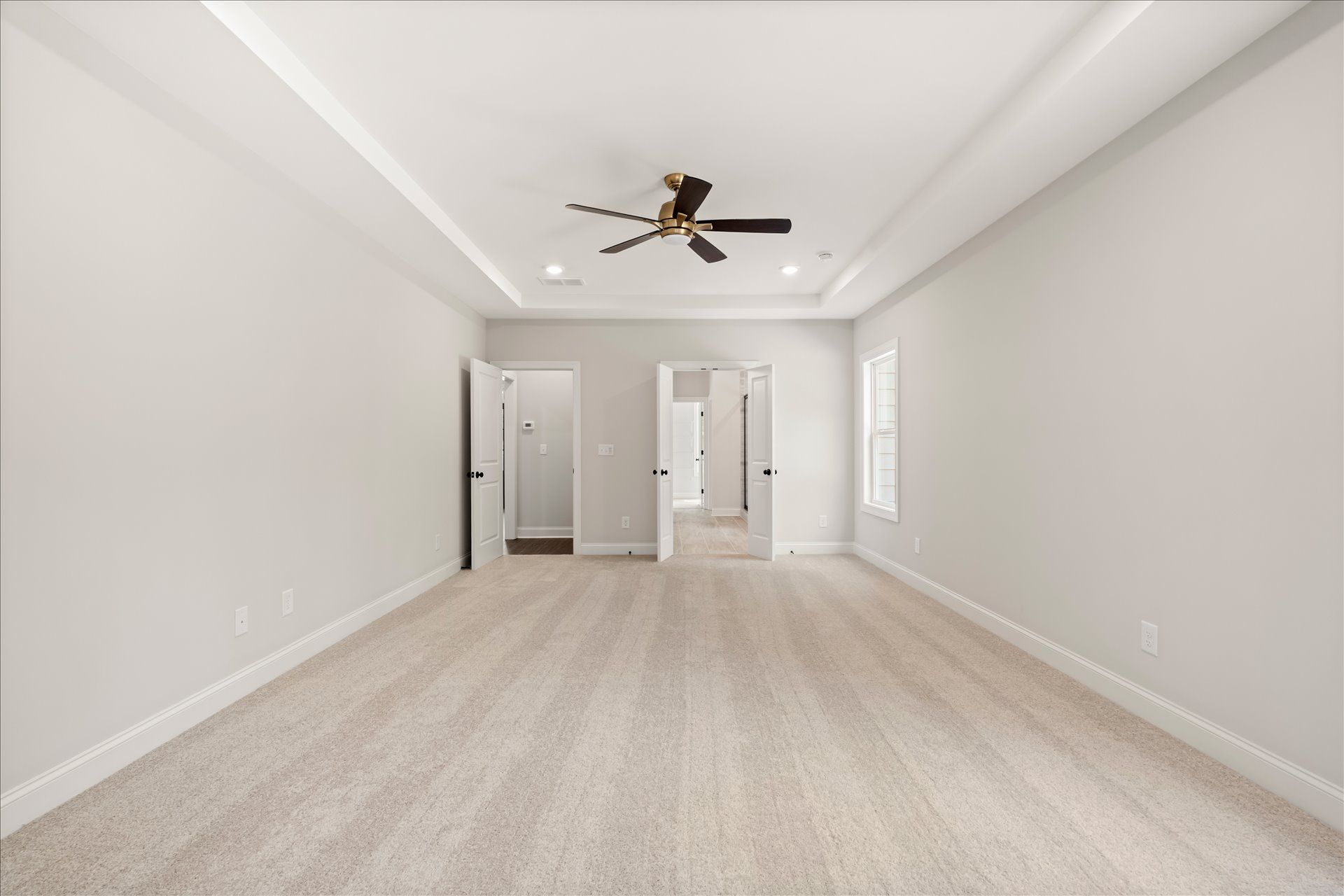Empty carpeted bedroom with white walls, ceiling fan, and open doors leading to a bathroom and closet.