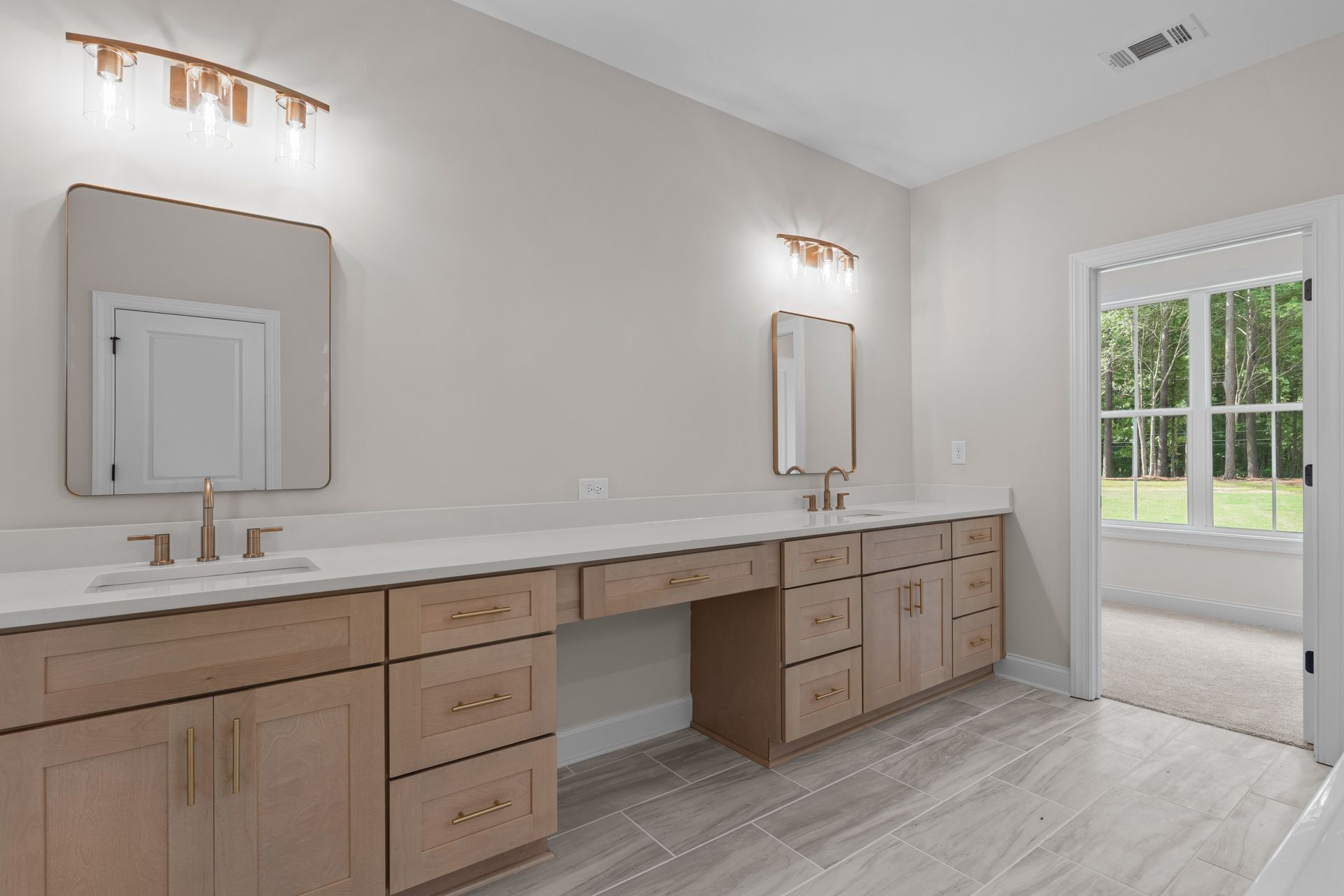 Modern double vanity bathroom with light wood cabinets, white countertop, and glass door to outside