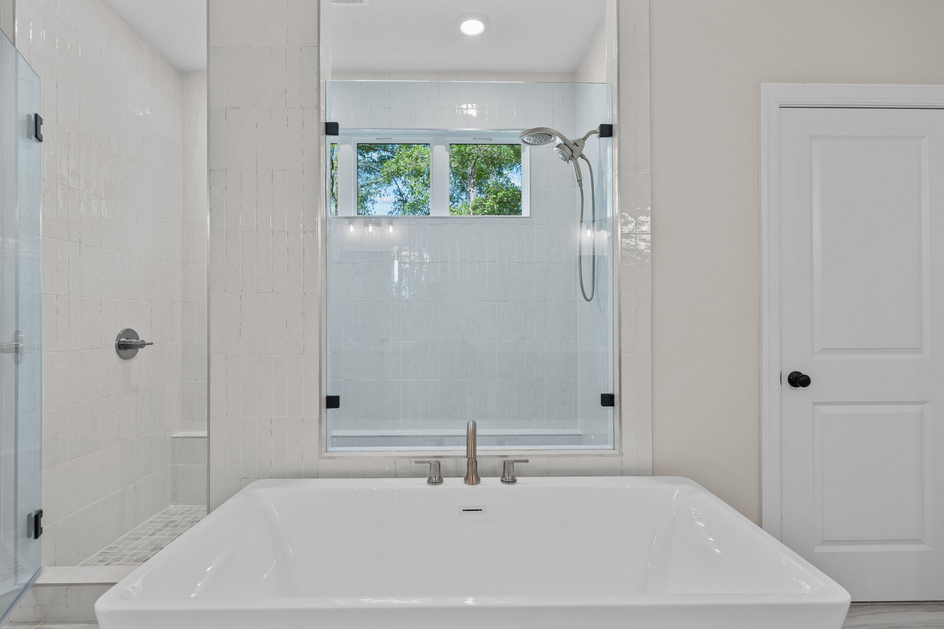 Bright white bathroom with soaking tub, glass shower, window, and two white doors