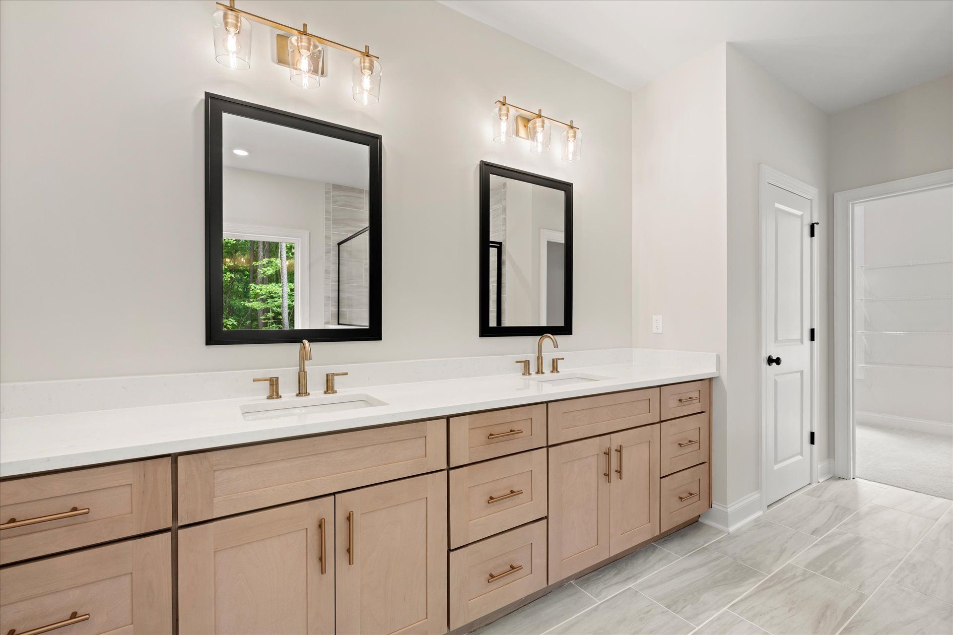 Modern bathroom vanity with double mirrors, brass sconces, and light wood cabinets