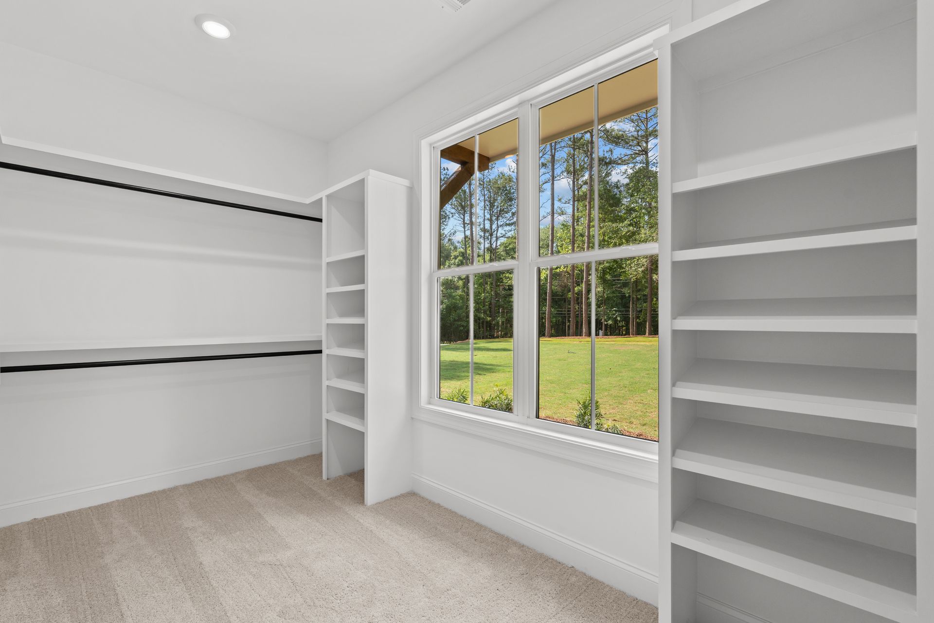 Bright empty walk-in closet with white shelves and a large window overlooking green grass.