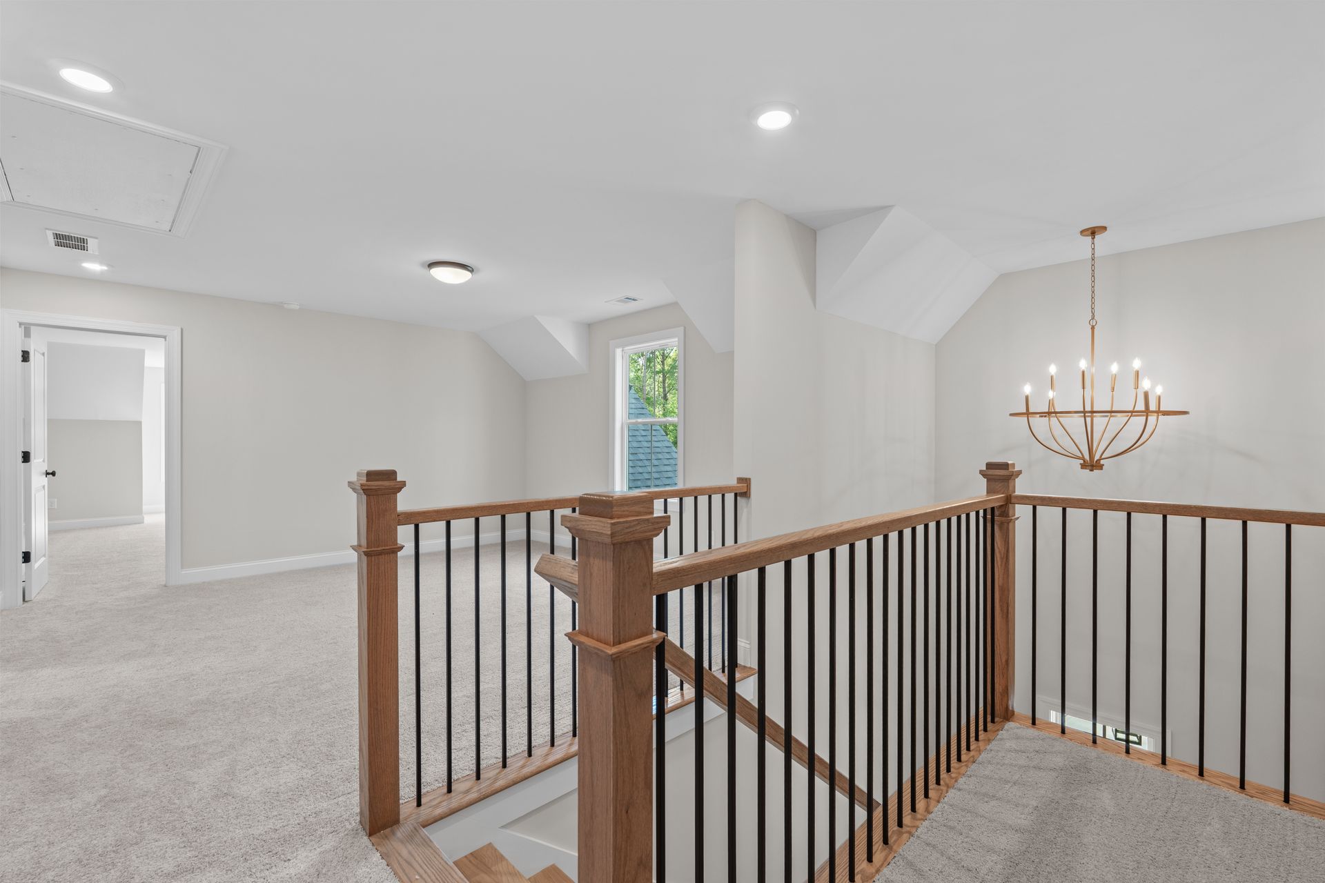 Bright carpeted upstairs landing with wooden railing and chandelier in a white home interior